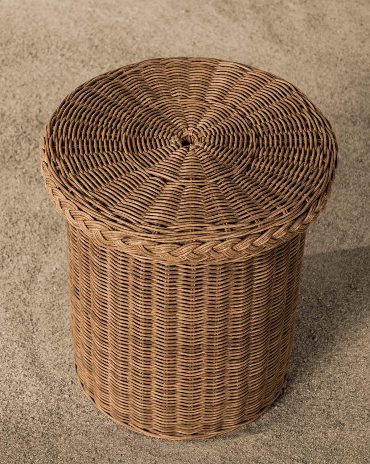 Close-up of the round Haviland Side Table in woven wicker on the upper right, with its textured pattern sharply detailed. A blurred background of light pebbles enhances this perfect piece for outdoor lounging, by McGee & Co.