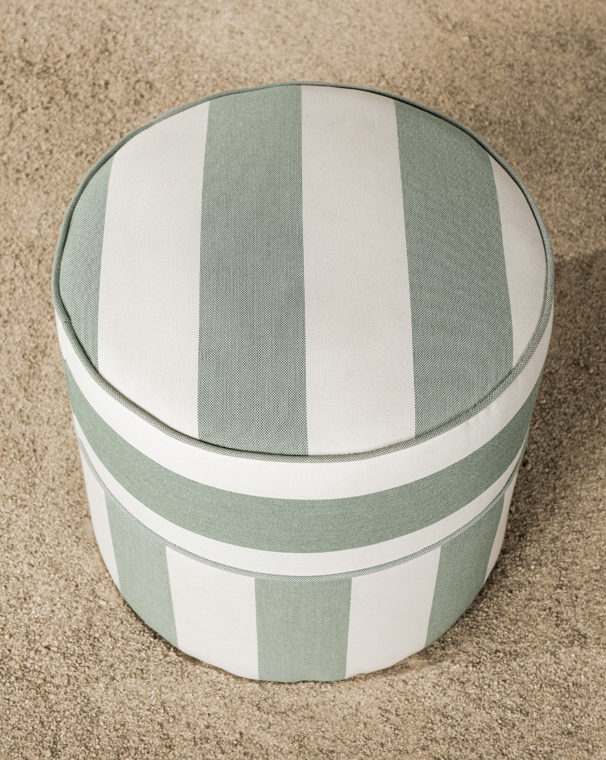 The Makerspalm Haviland Striped Ottoman features light green and white upholstery and sits on light-colored pebbles, offering a charming, weather-resistant addition to any patio or garden space. McGee & Co.