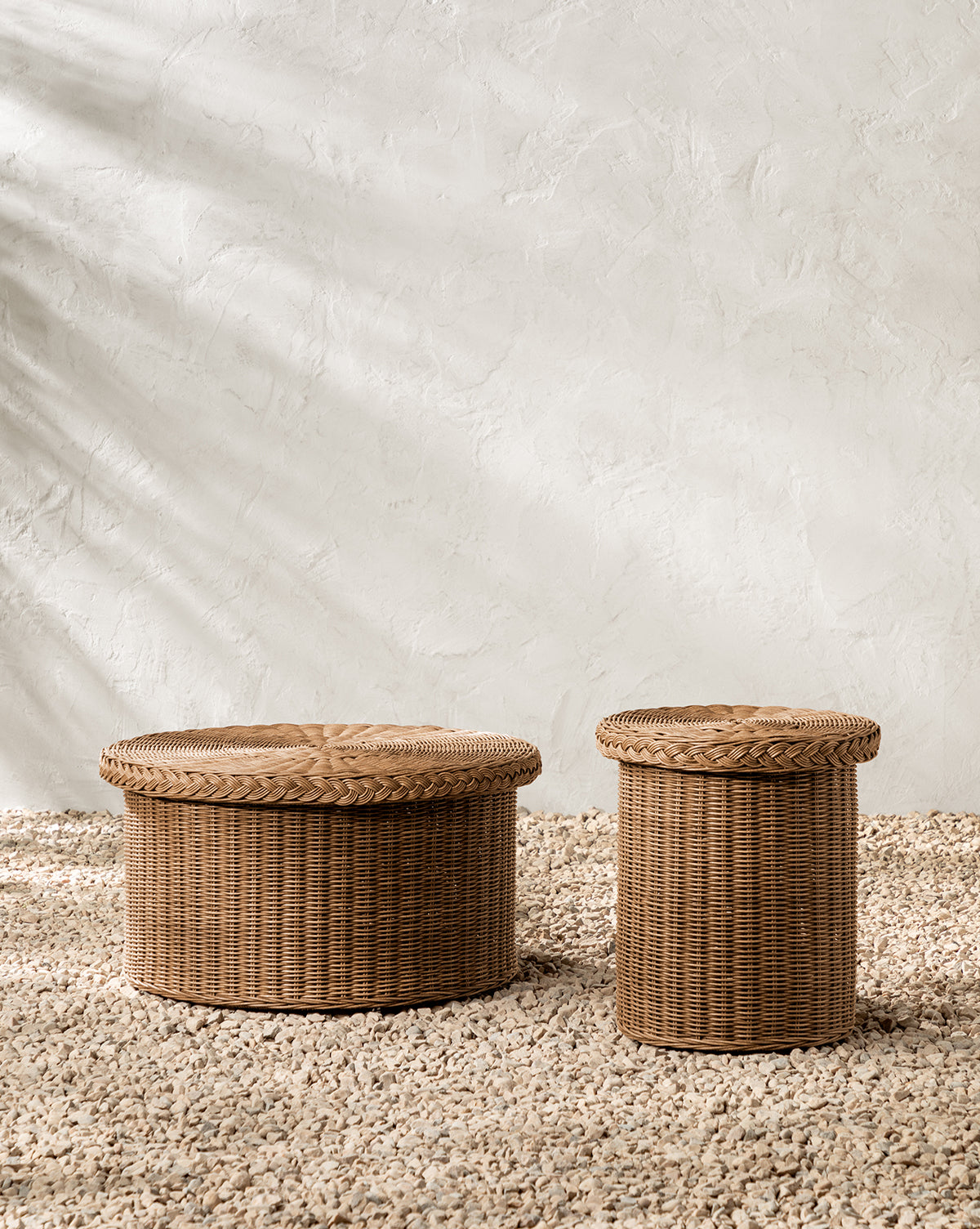 The Haviland Coffee Table, featuring two round wicker baskets with lids—one larger than the other—rests on a textured pebble floor against a light plastered wall with soft shadows, by McGee & Co.