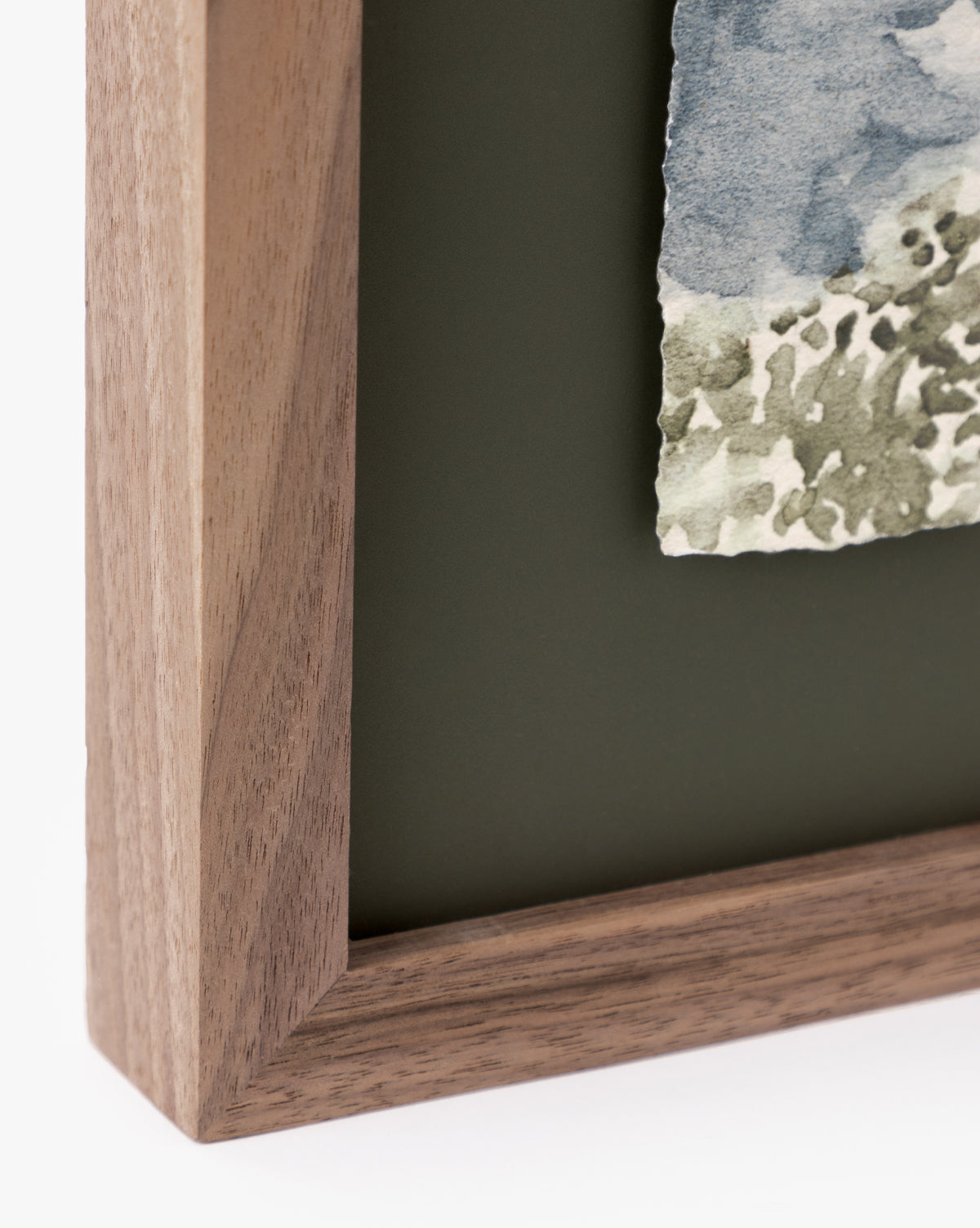 Close-up of a walnut frame corner around textured watercolor paper featuring abstract blue and green patterns from Head in the Clouds, mounted on a matte dark green background—ideal for lovers of cloudy day art.