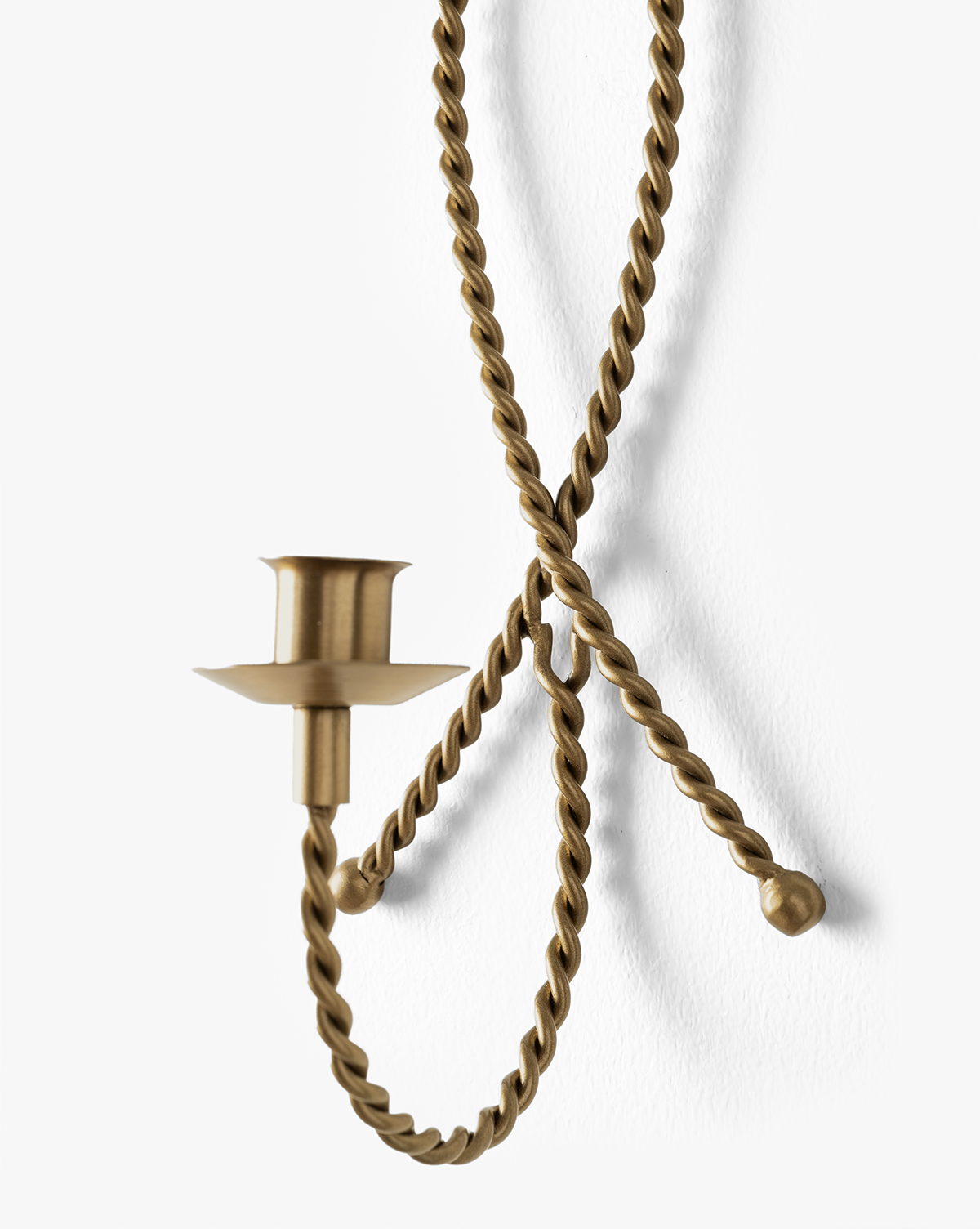 The Hearst Taper Holder is a wall-mounted, sculptural brass candle holder with a twisted, rope-like design, curled ends, and an empty candle cup, displayed against a white background, by McGee & Co.