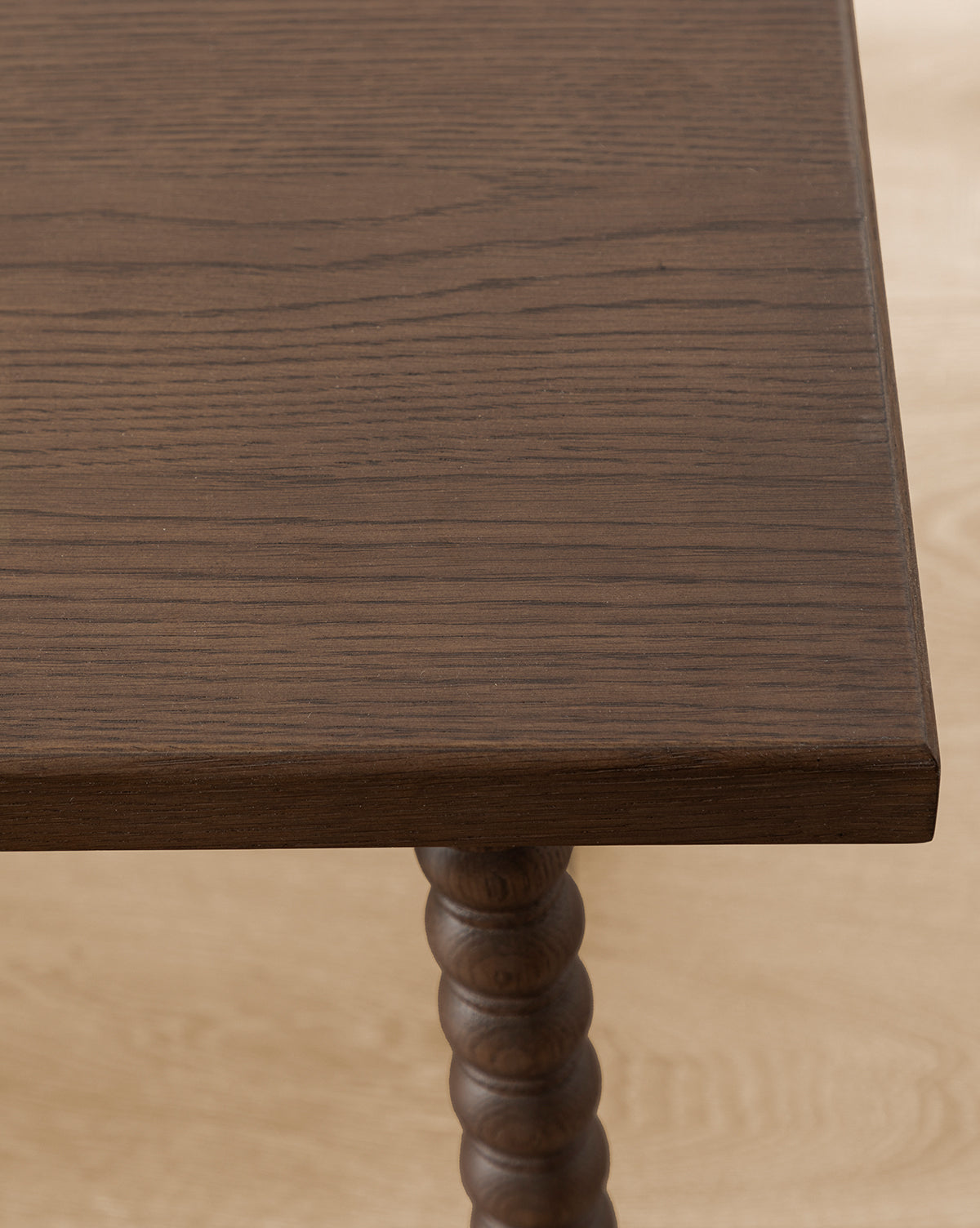 A close-up of the Heathcliff Bench highlights its dark walnut oak finish and distinct wood grain, featuring a corner of the tabletop and a decorative turned spiral leg, by McGee & Co.