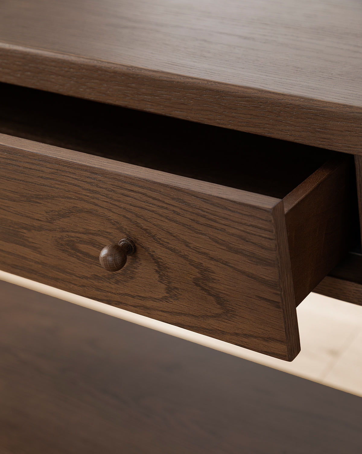 A close-up of the Heathcliff Console shows a partially open wooden drawer, featuring a round wooden knob and distinct wood grain patterns on its two-drawer design, by McGee & Co.