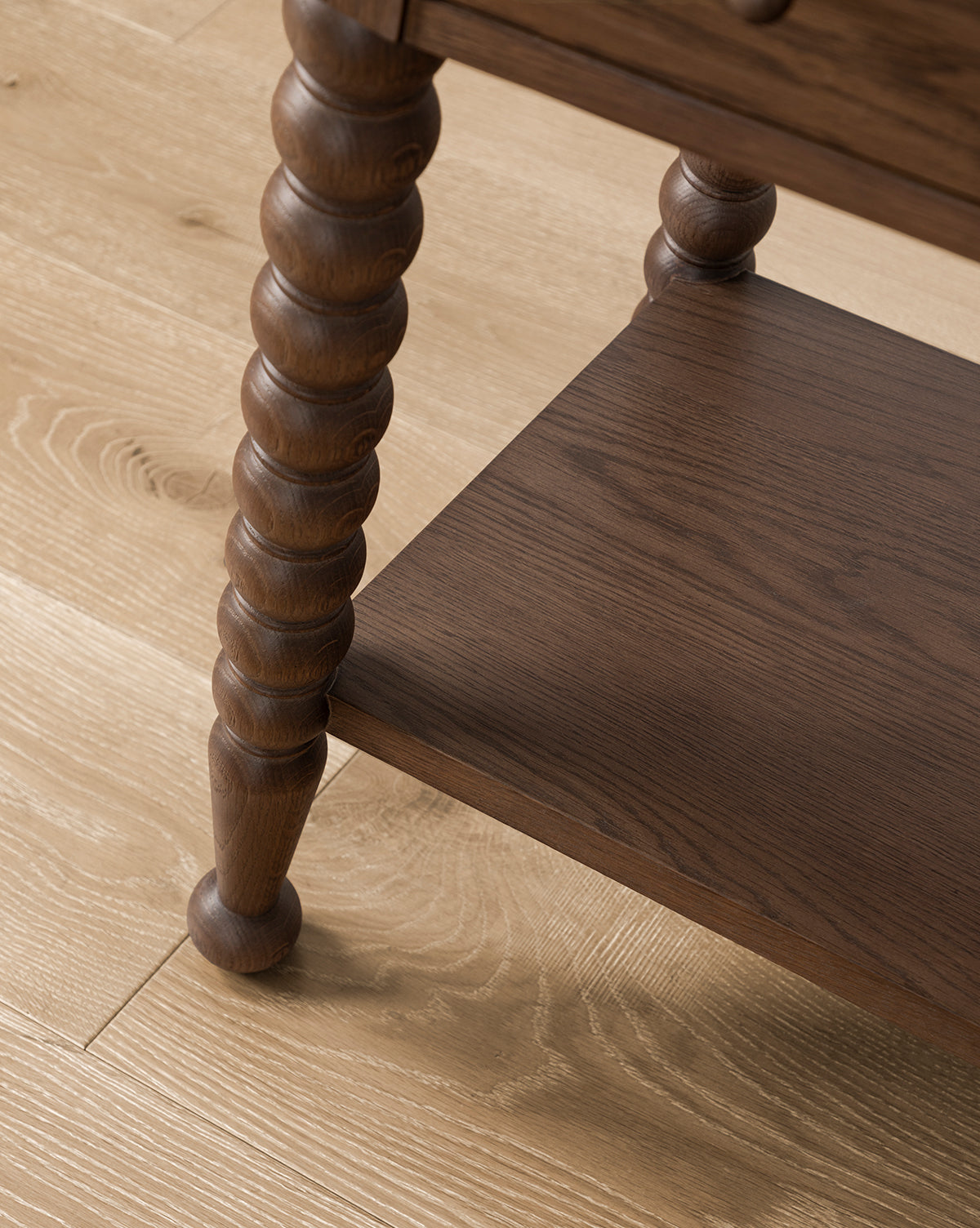 Close-up of the Heathcliff Consoles bobbin-style leg with turned detailing and lower shelf, displayed on a light wood floor, by McGee & Co.