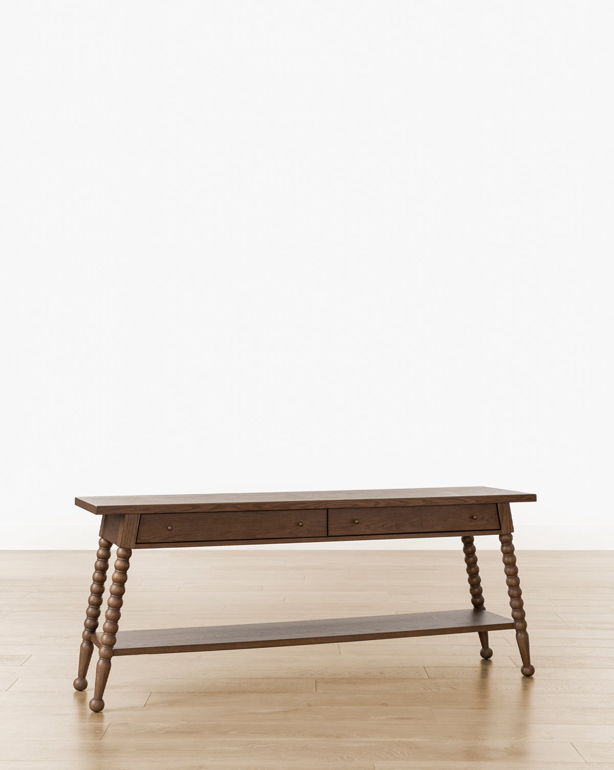 The Heathcliff Console, finished in walnut oak with two drawers, intricately turned bobbin-style legs, and a lower shelf, stands on a light wooden floor against a plain white background by McGee & Co.