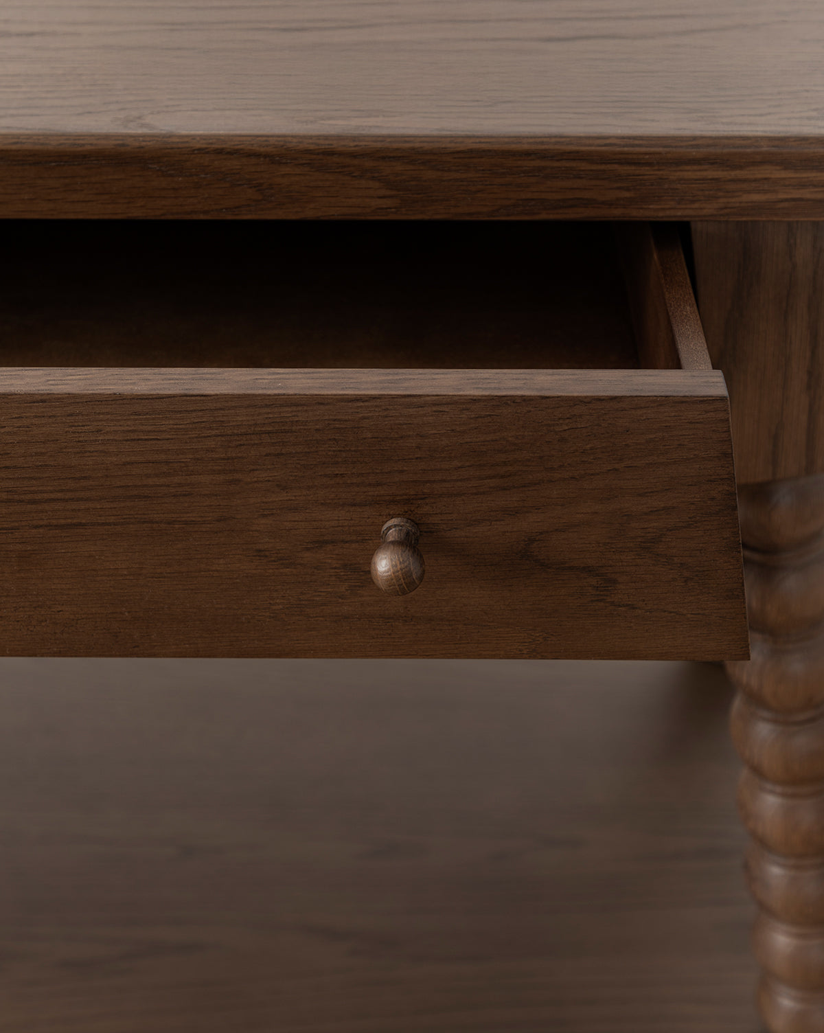 A close-up of the Heathcliff Console shows a partially open drawer with a round wooden knob and carved bobbin-style legs, all in a rich walnut oak finish, by McGee & Co.