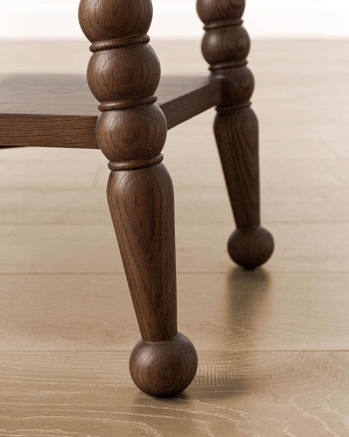 Close-up of two Heathcliff Console bobbin-style legs with a rounded, carved design, standing on a light wood floor. A lower wooden shelf is partially visible between the legs, by McGee & Co.