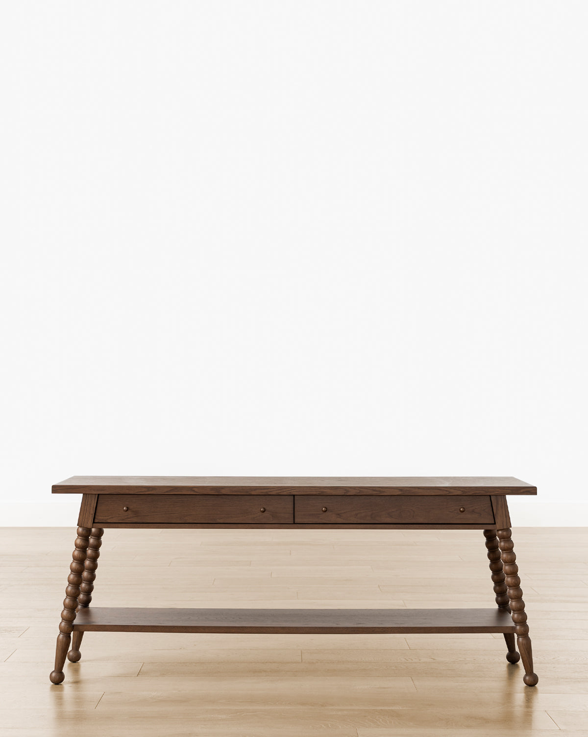 The Heathcliff Console features a dark walnut oak finish, two drawers, turned spindle legs, and a lower shelf, shown on a light wood floor against a plain white background, by McGee & Co.