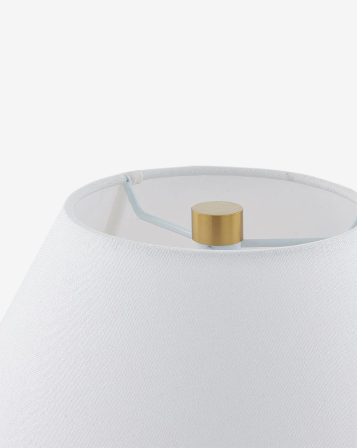 Close-up of the Helena Table Lamp highlighting its white linen shade, gold-colored finial, and visible metal support structure set against a plain, light background by McGee & Co.
