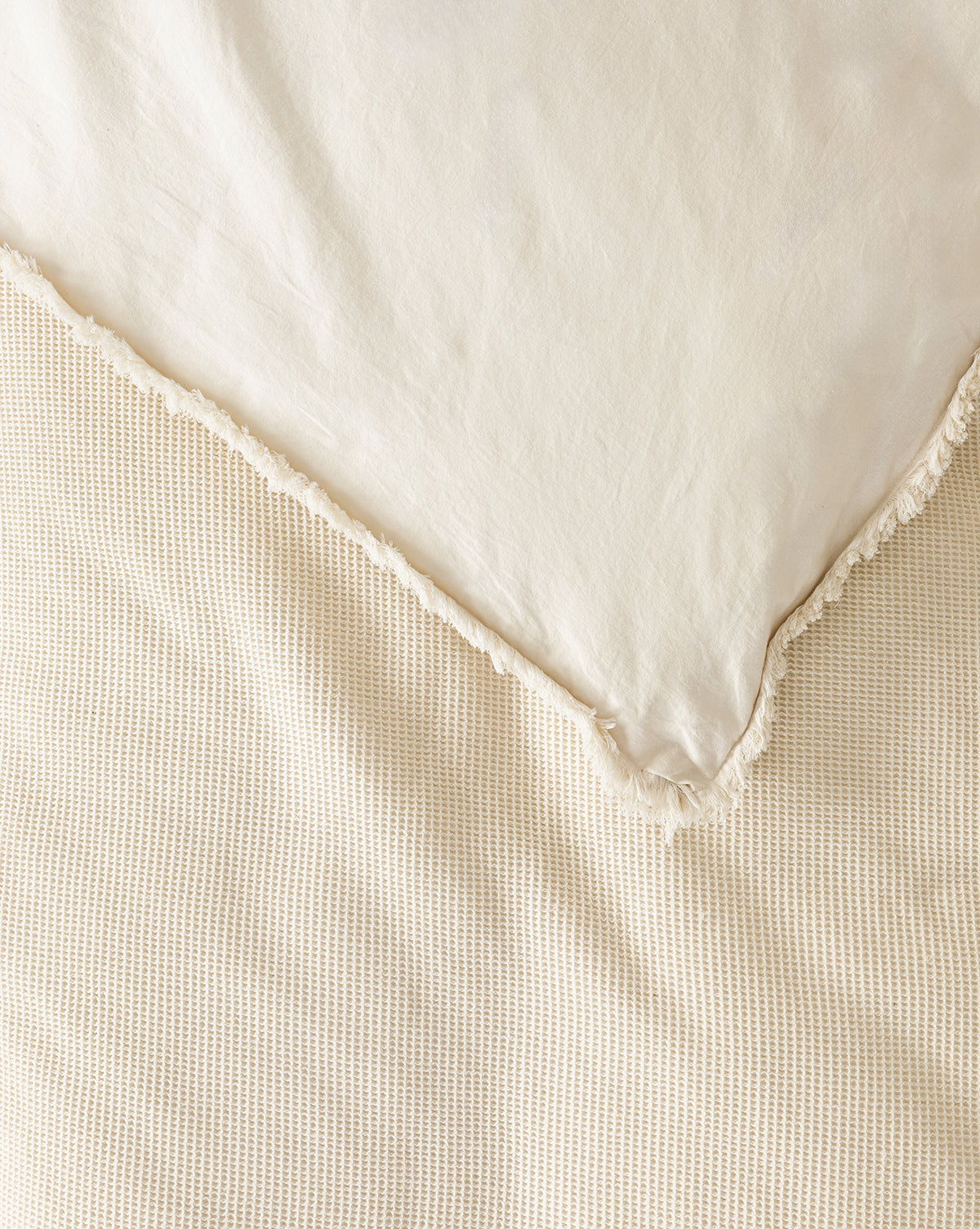 A close-up of a neatly made bed with the Helene Waffle Duvet Cover in cream cotton and a smooth pillow featuring subtle ruffle edging. The textured, cozy duvet cover and soft materials create an inviting, neutral look.