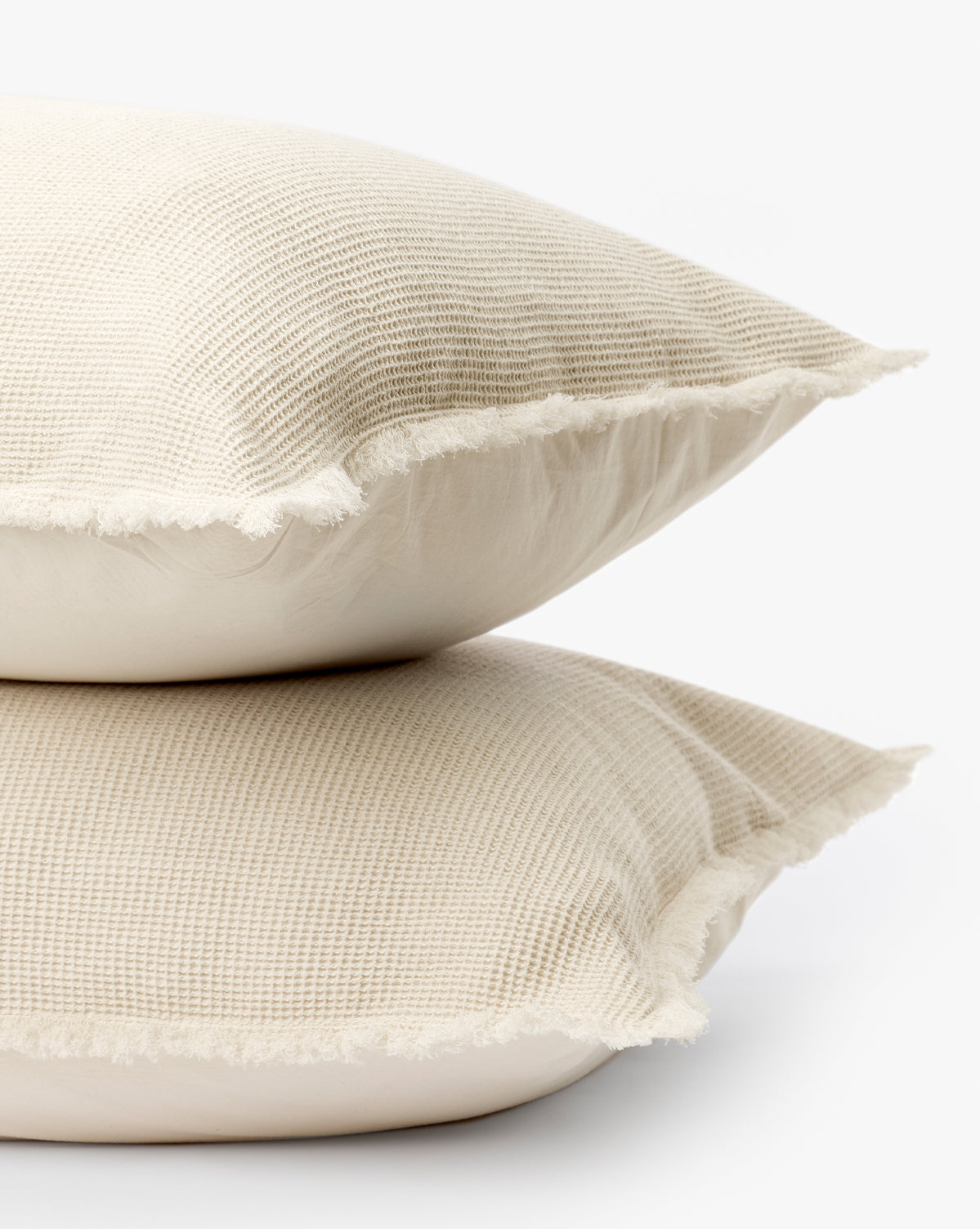 Two Helene Waffle Shams (Set of 2) in light beige, featuring a textured cotton waffle weave and fringed edges, are stacked together against a plain white background for an inviting, neutral look.