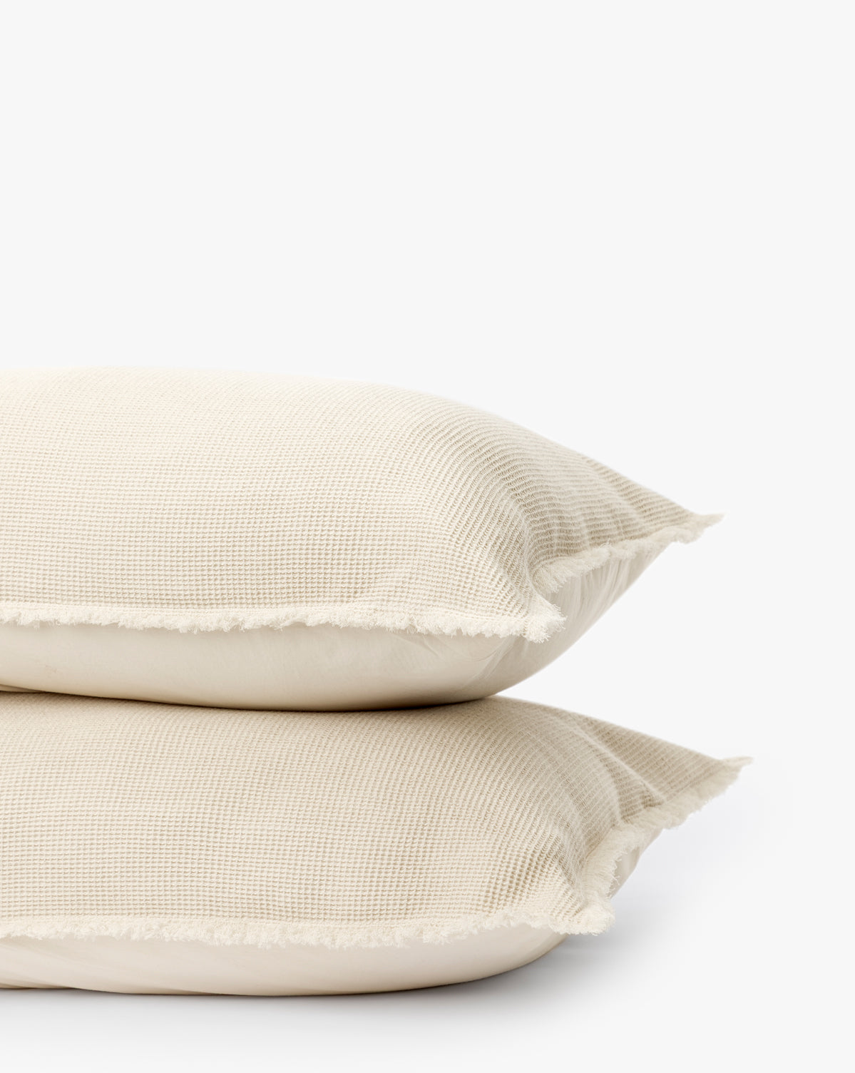 Two Helene Waffle Shams (Set of 2) in beige, featuring a soft cotton waffle weave and fringed edges, are stacked together against a plain white background to highlight their neutral textured design.