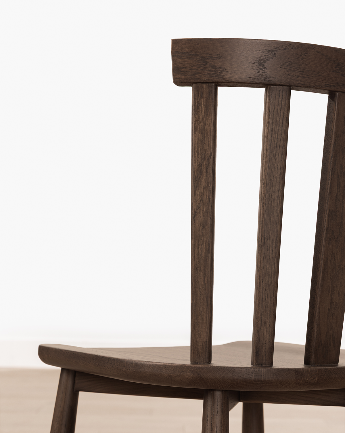 Close-up of the Hemingway Chair, featuring solid wood construction, a curved backrest, and vertical slats, set against a plain white background and light wood floor, by McGee & Co.