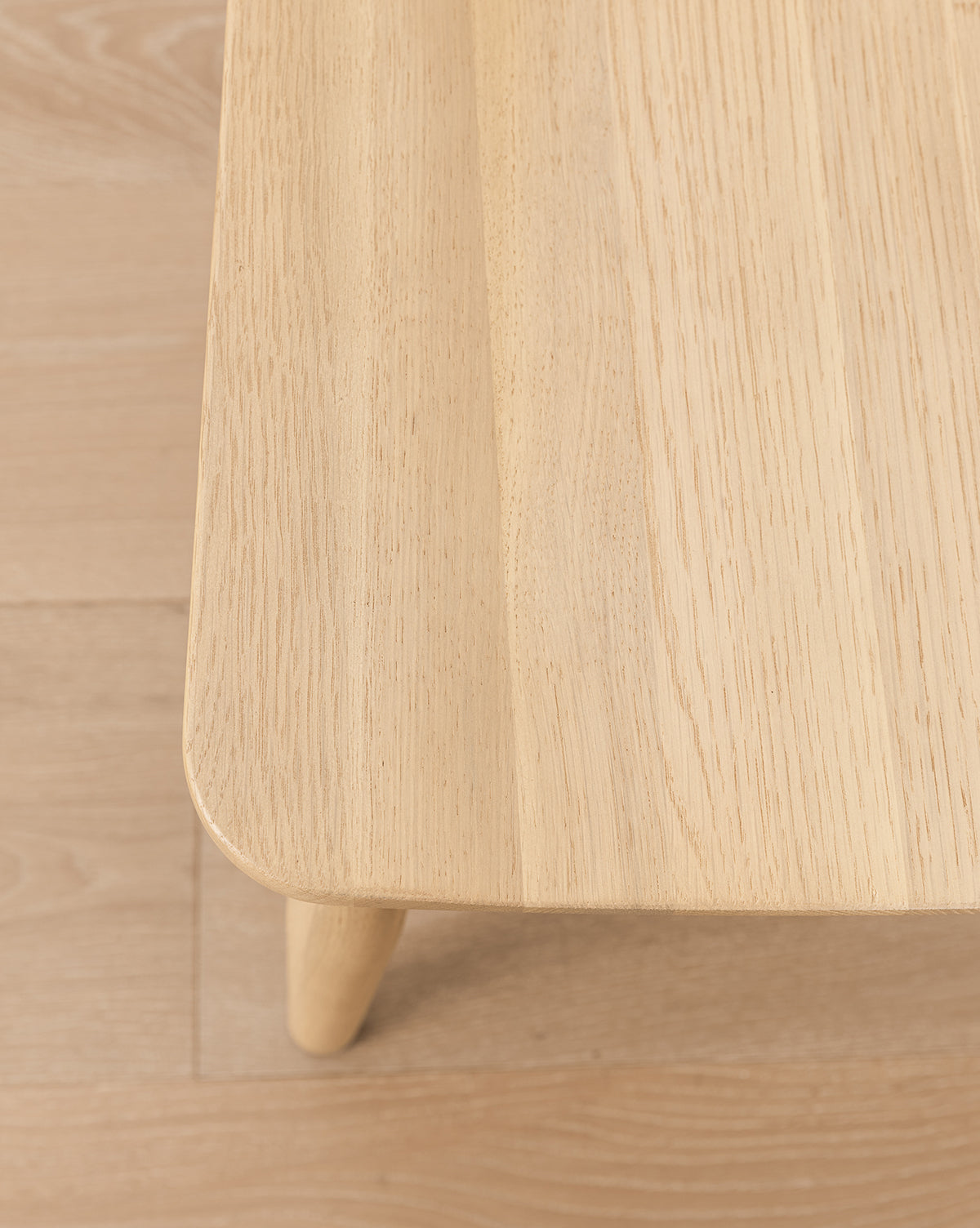 A close-up of a solid wood table with rounded edges and rich grain on a matching floor—pairs seamlessly with the elegant Hemingway Stool for any kitchen or dining space, by McGee & Co.