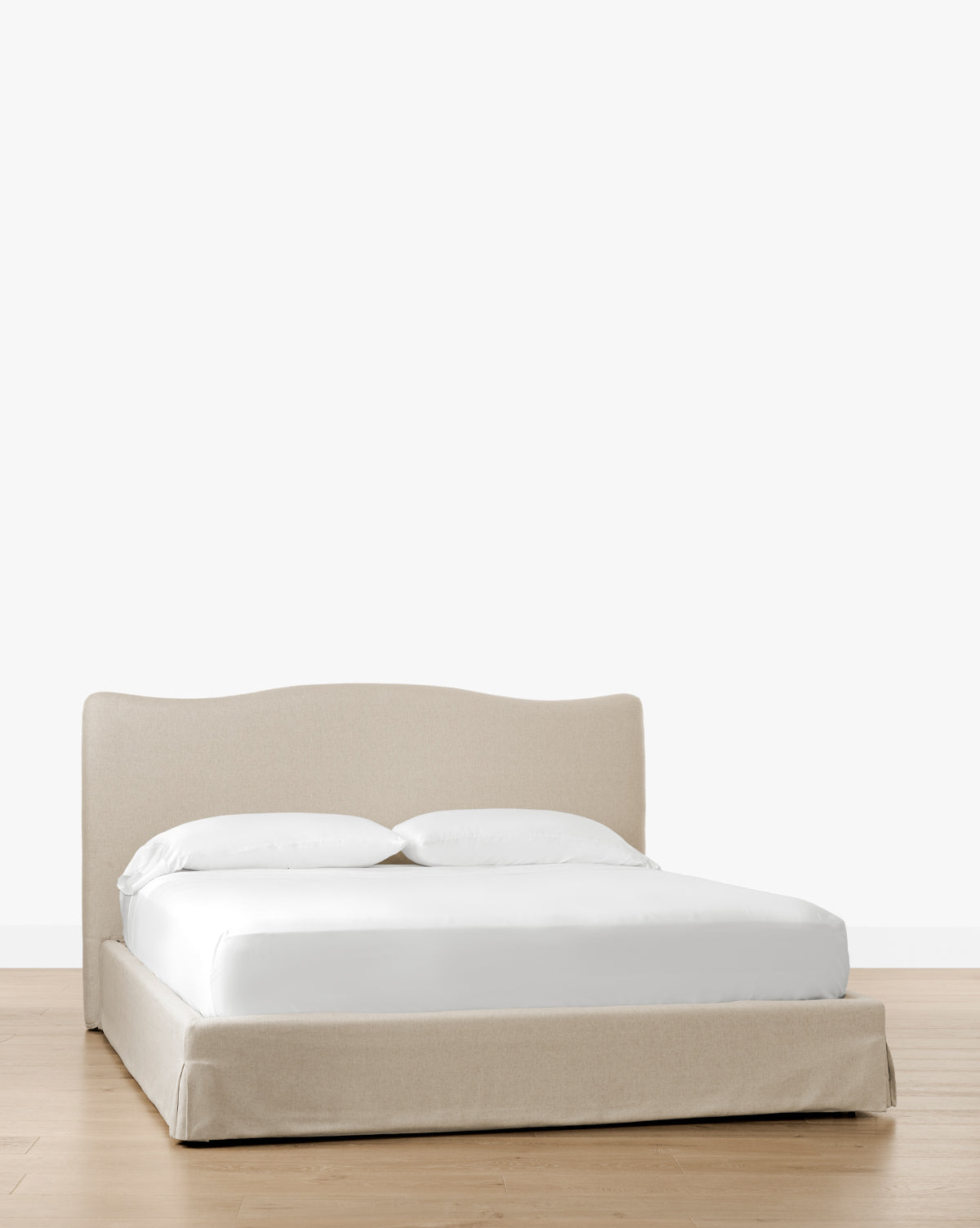 The Henrietta Bed (Ready to Ship), featuring beige upholstery and a low curved headboard, offers effortless bedroom styling with white bedding on a light wooden floor against a plain white background, by McGee & Co.