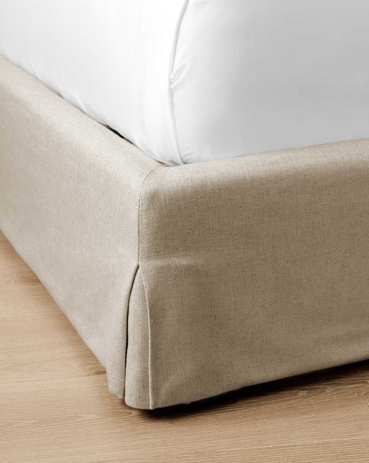Close-up of the corner of the Henrietta Bed (Ready to Ship) in beige upholstery with a white bedsheet, set on a light wooden floor—a stylish detail for effortless bedroom decor, by McGee & Co.