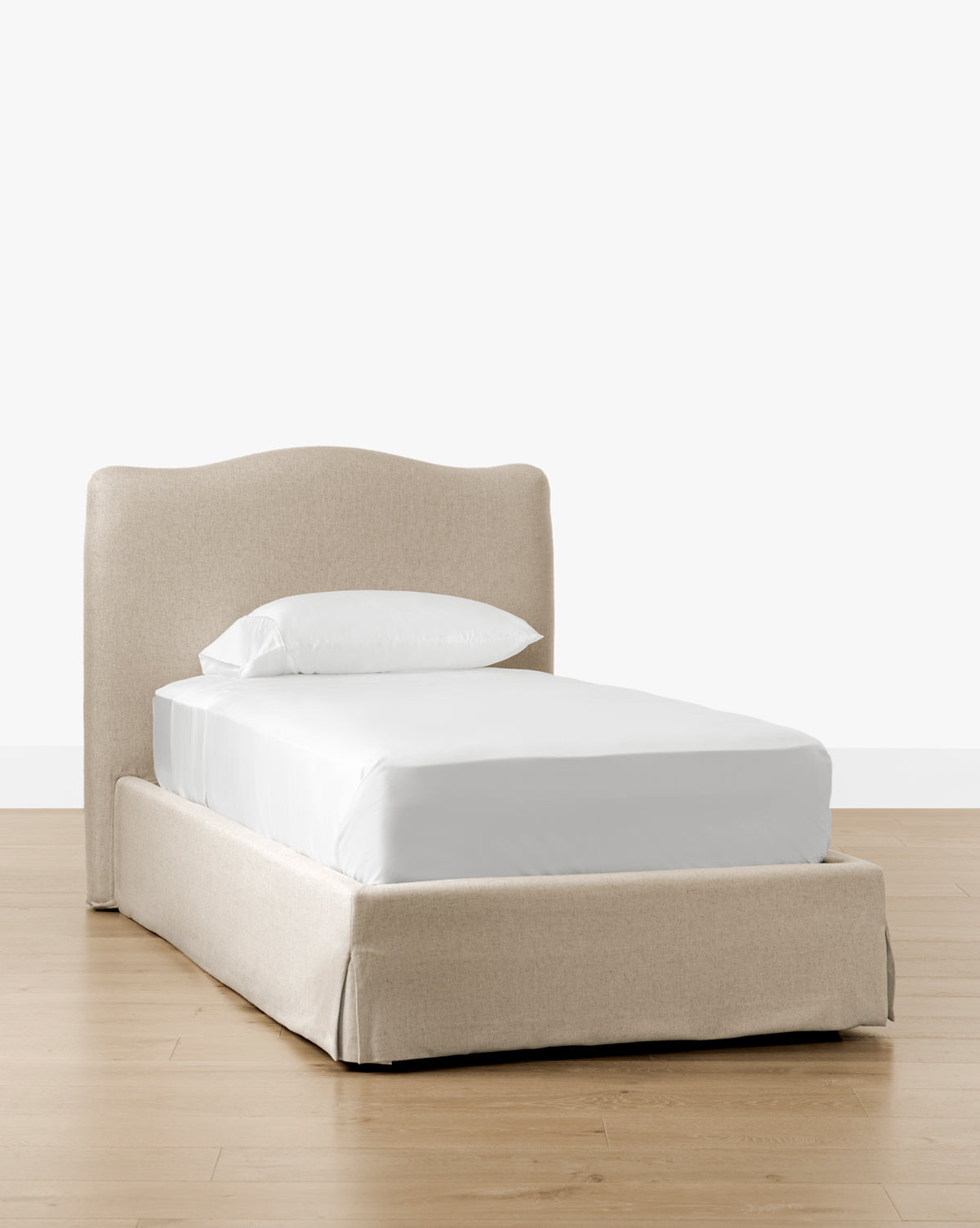 The Henrietta Bed (Ready to Ship), featuring beige upholstery and a curved headboard, is shown with white bedding on a light wood floor—an elegant choice for bedroom styling against a plain white background, by McGee & Co.