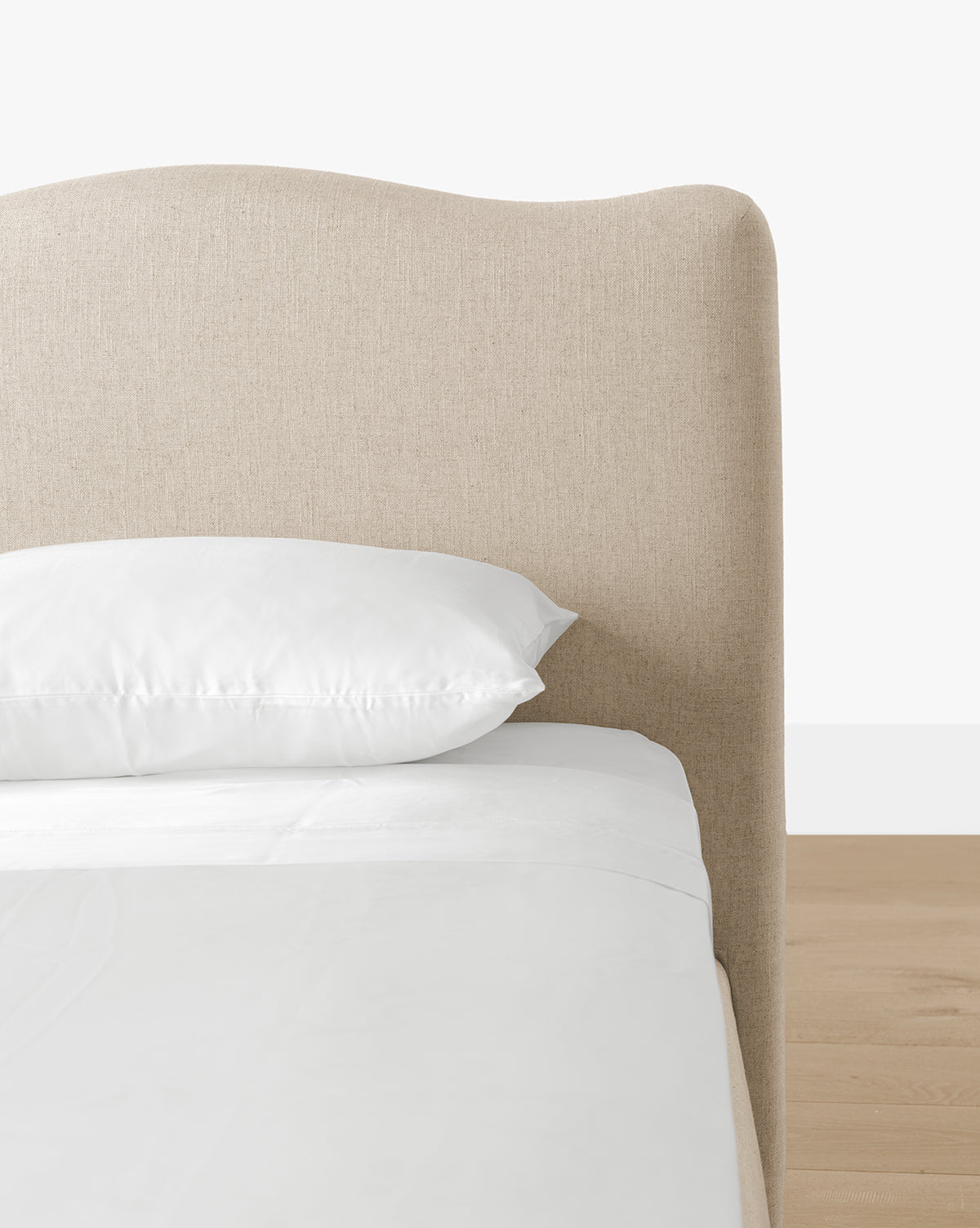 The Henrietta Bed (Ready to Ship) features a beige curved upholstered headboard, white pillow and bedding, set on a light wood floor—an elegant choice for stylish bedrooms with a clean, modern look, by McGee & Co.