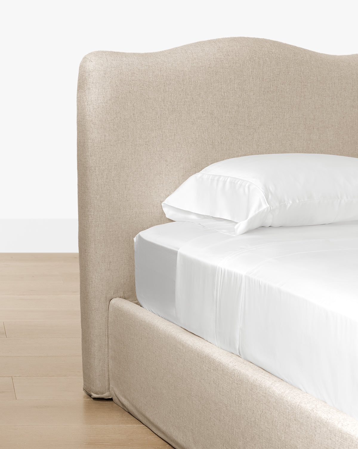 A close-up of the Henrietta Bed (Ready to Ship) showcases its beige curved upholstered headboard and frame, neatly made with white sheets and pillow on a light wood floor—ideal for elegant bedroom decor, by McGee & Co.