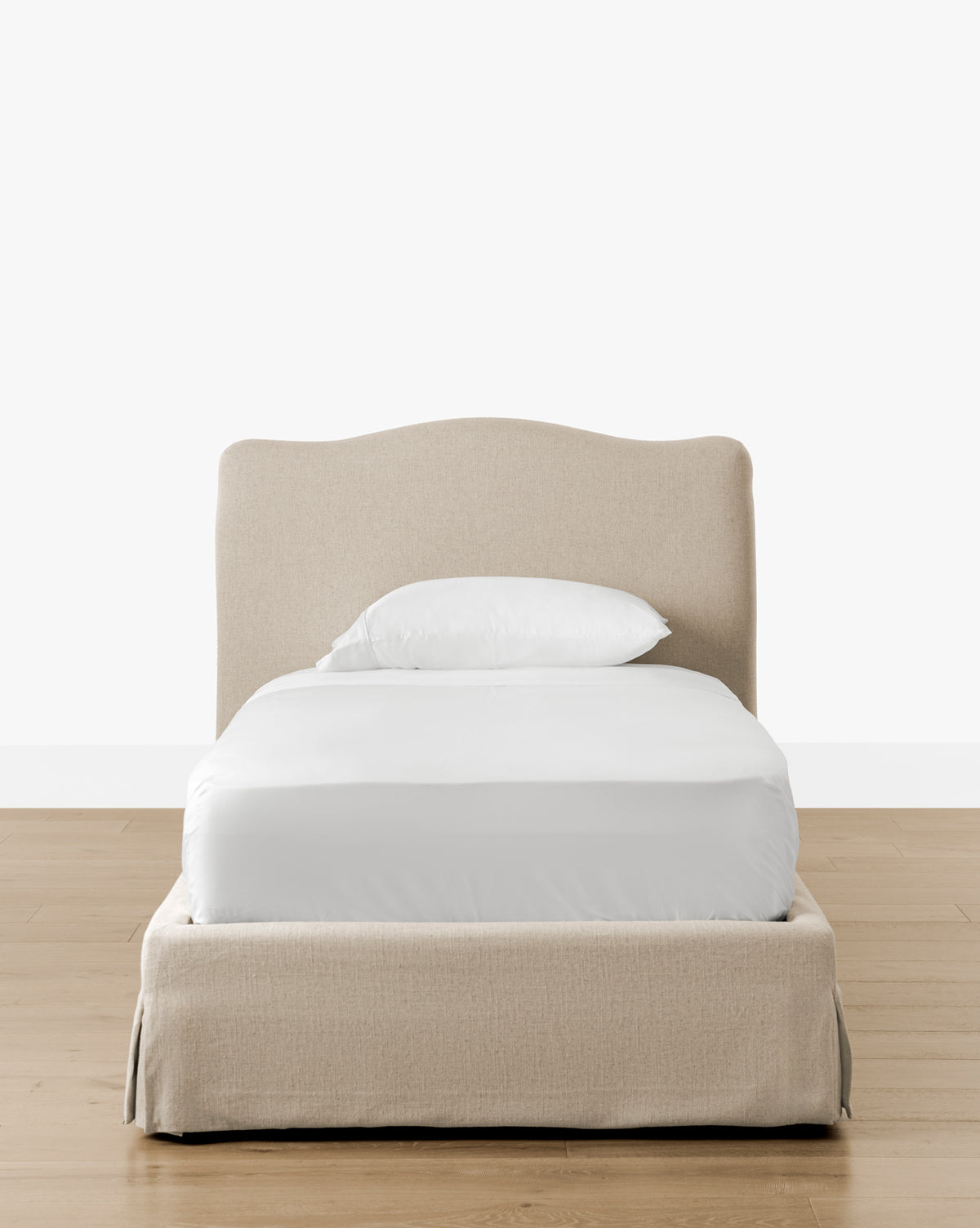 The Henrietta Bed (Ready to Ship), featuring beige upholstery and a curved headboard, is dressed in white bedding with a single pillow, set on a light wood floor against a plain white background—perfect for refined bedroom styling by McGee & Co.