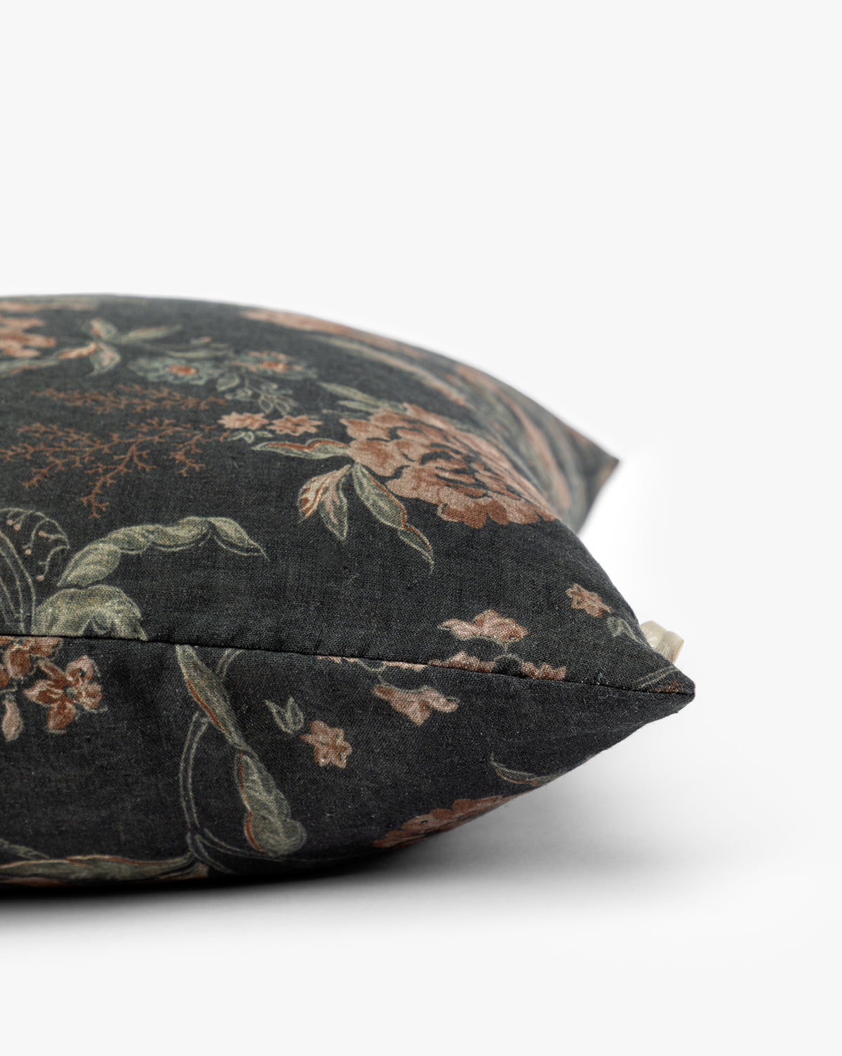 A close-up side view of the Hestercombe Pillow Cover, a vintage-inspired decorative pillow with dark fabric showcasing an intricate floral pattern in muted green and brown on a white background, by McGee & Co.