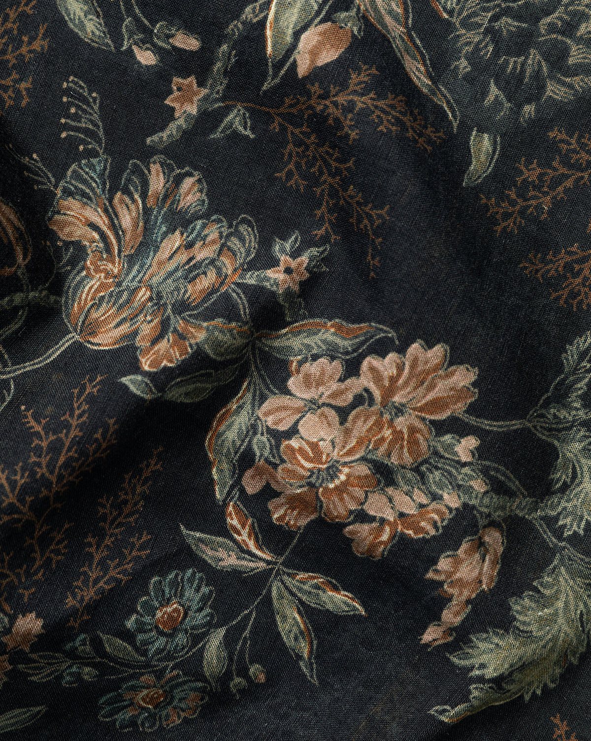 A close-up of the Hestercombe Tablecloth shows its dark fabric with a detailed vintage floral pattern in peach, green, and beige. The slightly wrinkled texture adds depth to the botanical design, by McGee & Co.