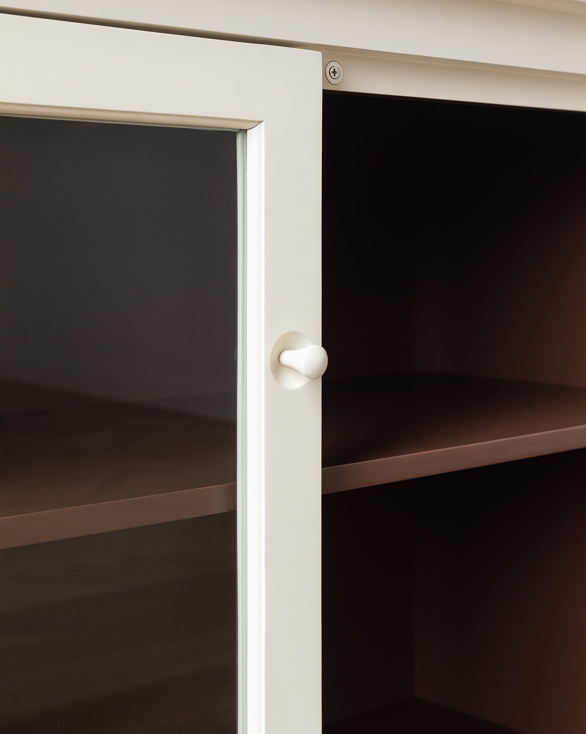 Close-up of the Highgate Cabinet in bone white, inspired by Victorian furniture, featuring a glass door, round white knob, and empty brown shelves inside, by McGee & Co.