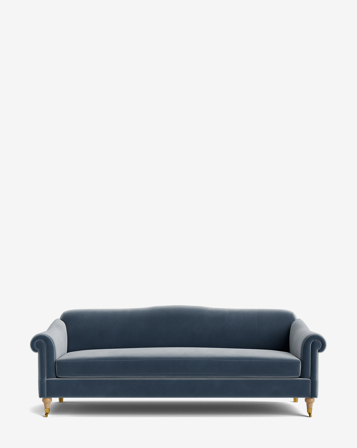 The Hildegard Sofa 90 is a blue velvet handcrafted sofa with rolled arms, a gently curved back, and wooden legs with brass casters, shown against a plain white background by McGee & Co.