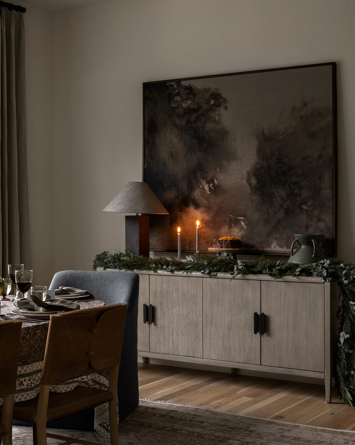 A cozy dining room showcases a set table, sideboard with lit candles and greenery, lamp, and the striking Spilled Ink abstract wall art above, creating a warm, inviting atmosphere.