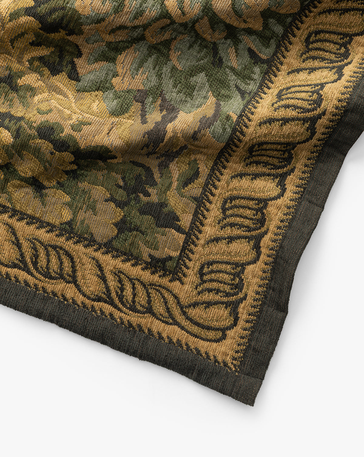 A close-up of the Hortensia Wall Tapestry shows a woven floral and leafy pattern in green, gold, and black tones with an intricate decorative border framing the textiles corner, by McGee & Co.