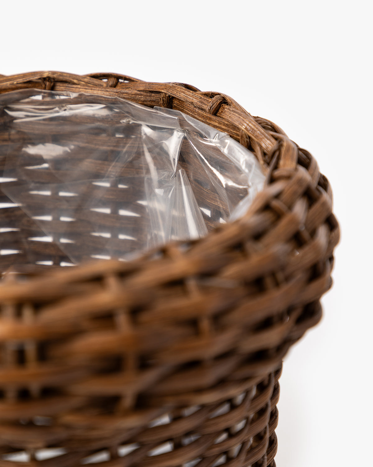 A close-up of the Huger Woven Planter, a brown woven basket featuring a clear plastic liner inside, set against a plain white background, by McGee & Co.
