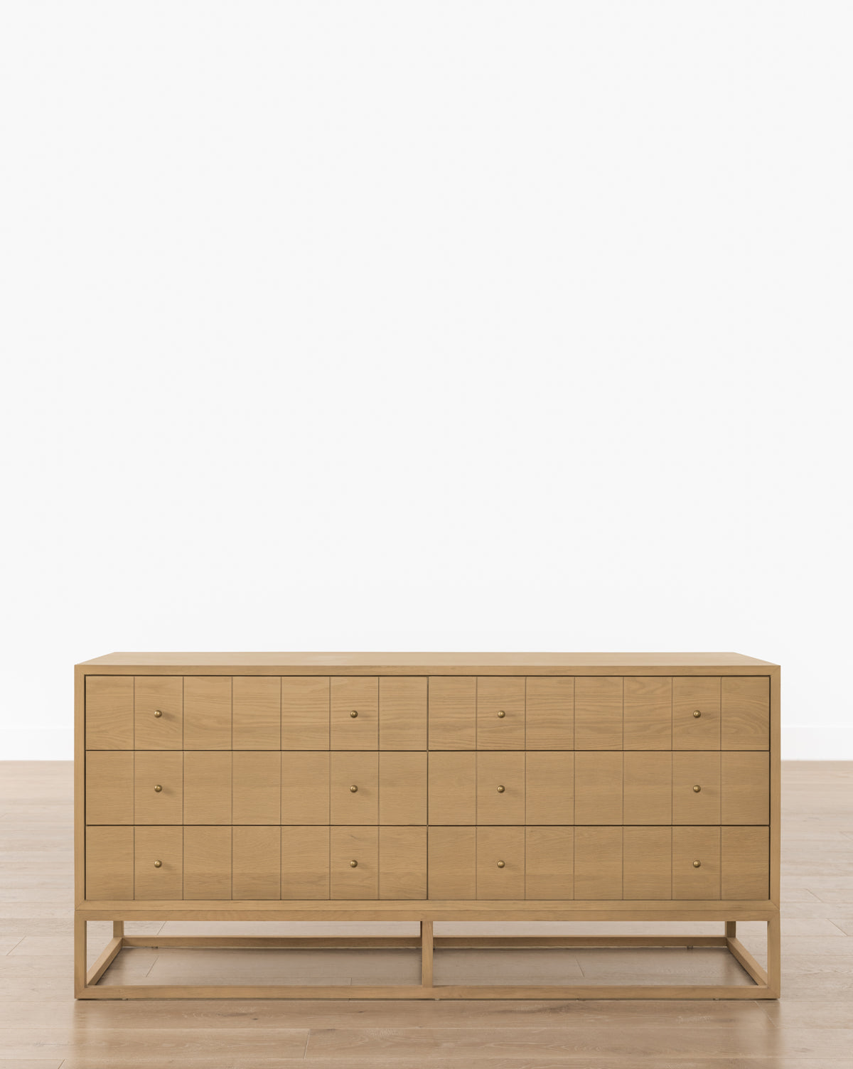 The Huxton Dresser is a modern piece with 18 small square drawers, each with minimalist round knobs, and an etched grid pattern. It stands on an open rectangular base, complementing light wood floors and a plain white wall by McGee & Co.