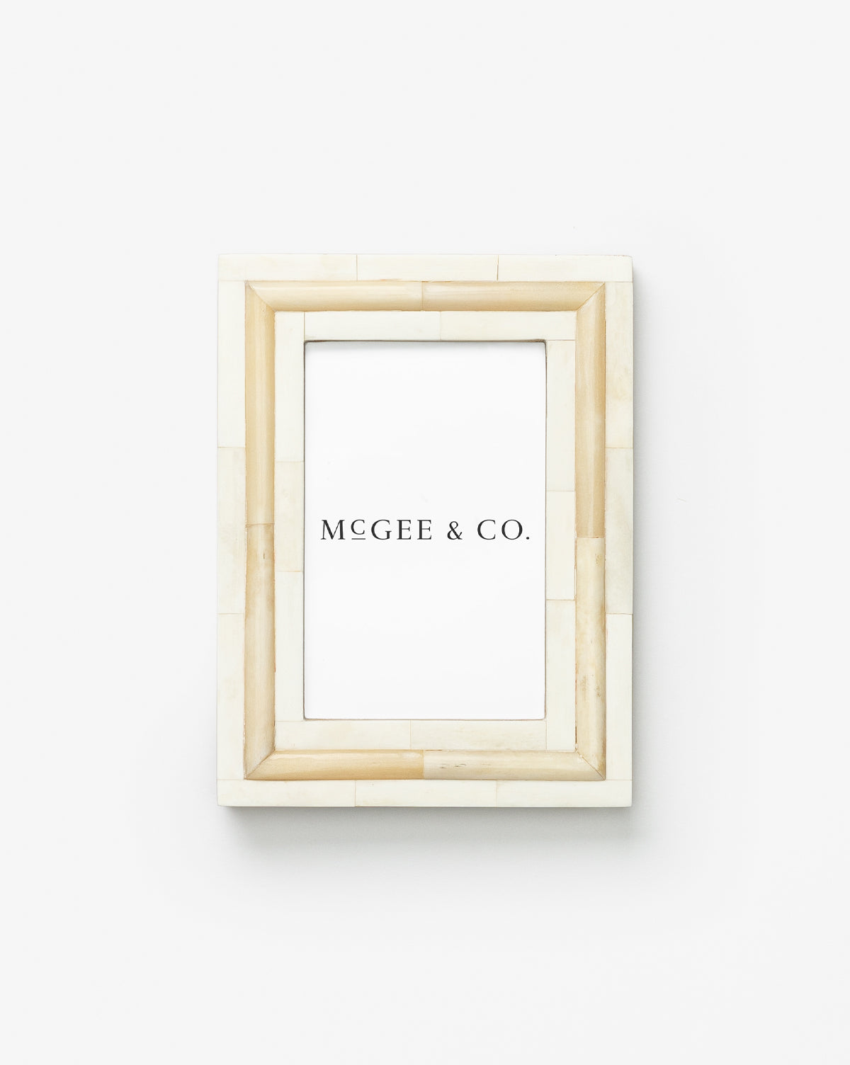 An off-white, rectangular Inlay Bone Frame with a tiled bone trim, crafted from engineered wood, is shown vertically on a plain white background and contains a placeholder print labeled MCGEE & CO. in black text.