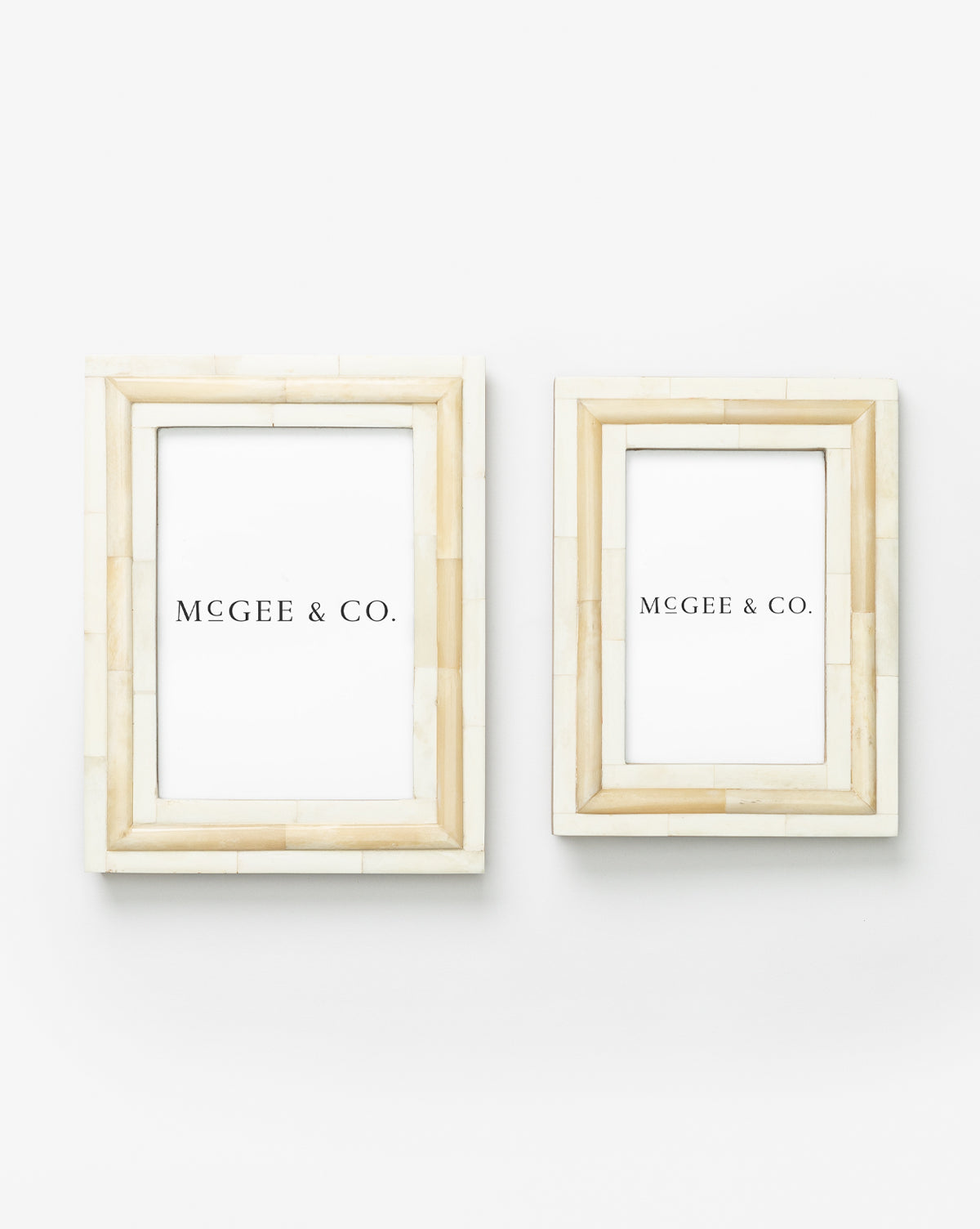 Two Inlay Bone Frames, crafted from engineered wood in beige and ivory with white inserts reading MCGEE & CO., are mounted side by side on a plain white wall, the left frame slightly larger than the right.