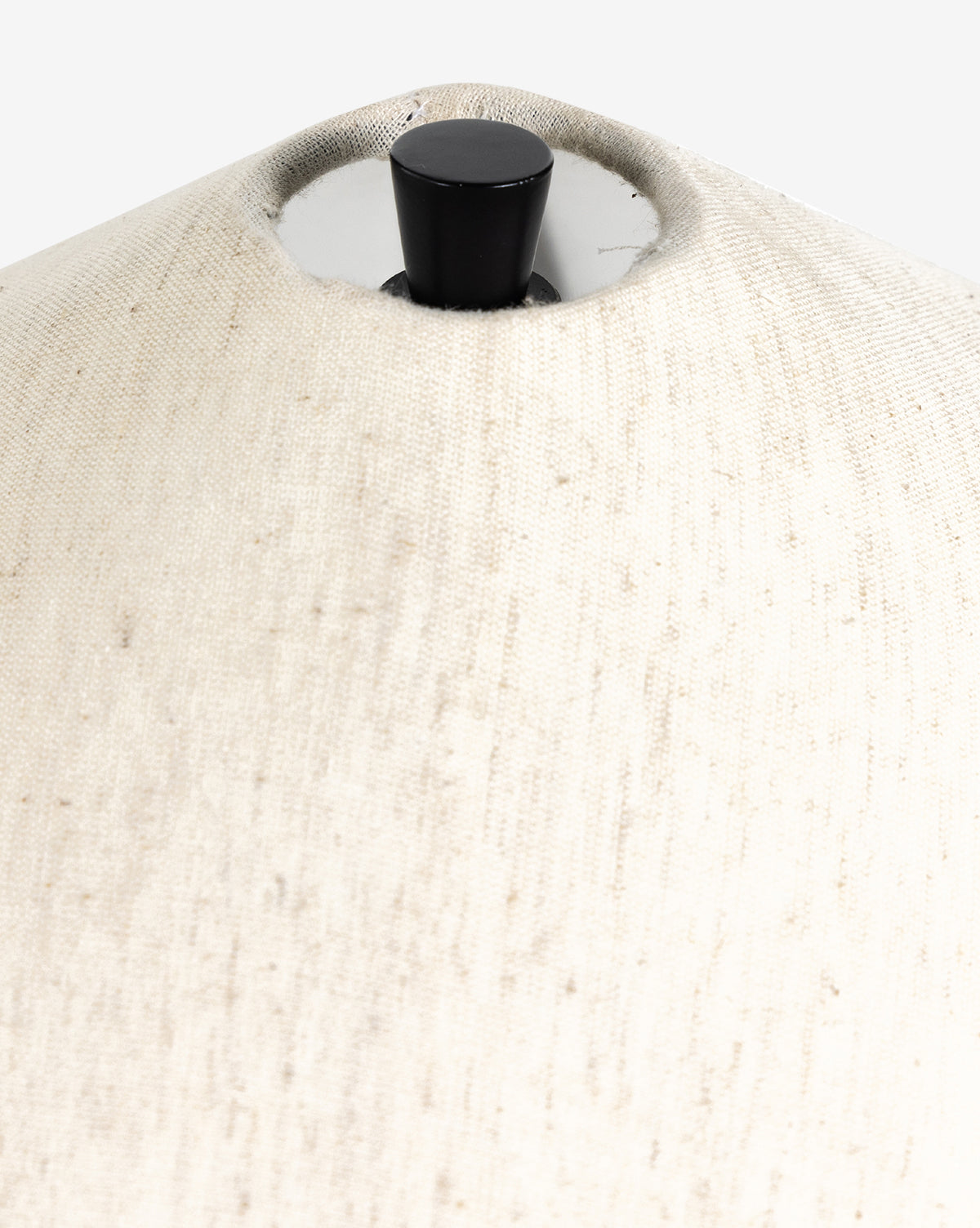 Close-up of the top part of the Innes Tapered Table Lamp’s light beige fabric shade with a black finial and silver hardware at the center, complementing décor such as a basket weave mirror, by McGee & Co.