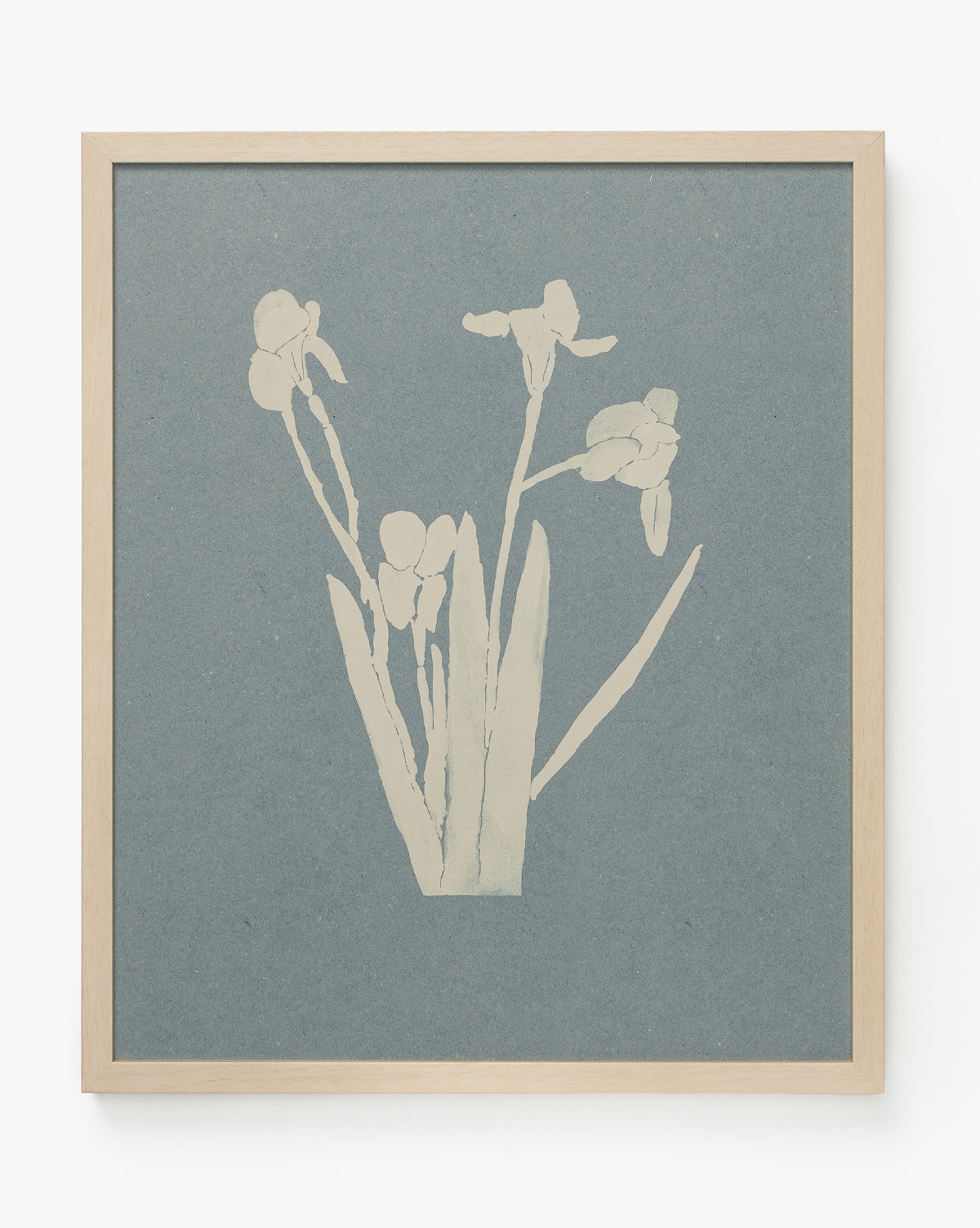 The Iris Ink Block is a minimalist botanical artwork with white silhouettes of long-stemmed flowers and leaves on a muted blue-gray background, perfect as blue and white wall decor and framed in light wood, by McGee & Co.