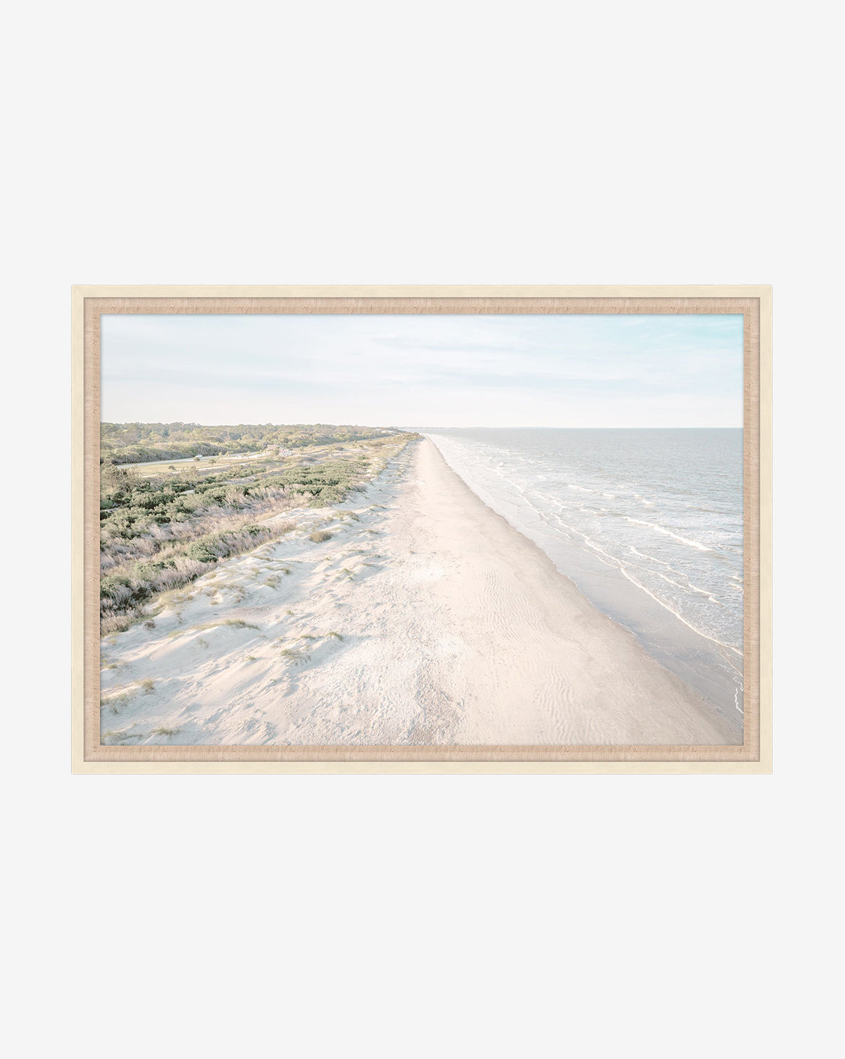 The Isle Stretch is a gallery-quality giclee print in a neutral wood frame, featuring an aerial view of a sandy beach with gentle ocean waves and lush greenery—perfect for bringing serene coastal beauty to any space, by McGee & Co.