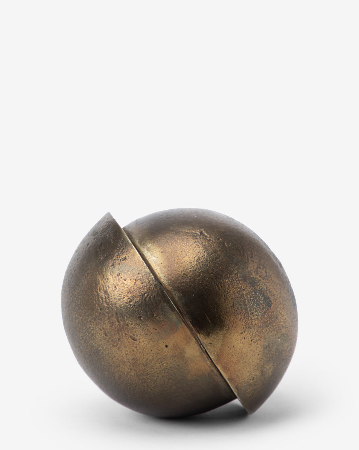 The Jackson Offset Sphere is a round, metallic decor piece with a weathered brass finish and a bold diagonal cut. Its modern design stands out on a white surface against a plain background.