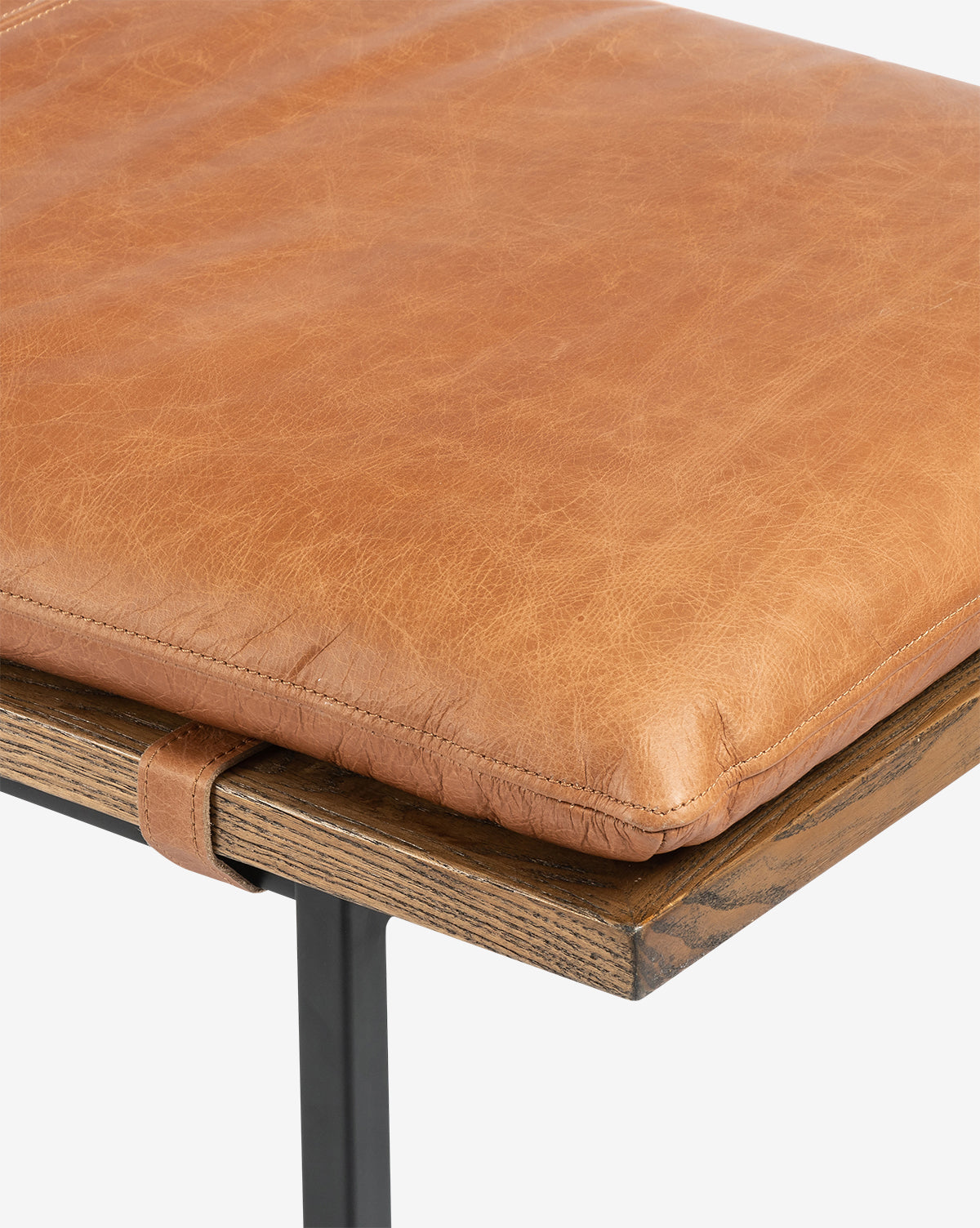 Close-up of the Jagger Accent Bench featuring a tan leather seat cushion, secure strap detail, and sturdy black metal legs, showcasing the leather texture on this transitional piece, by McGee & Co.