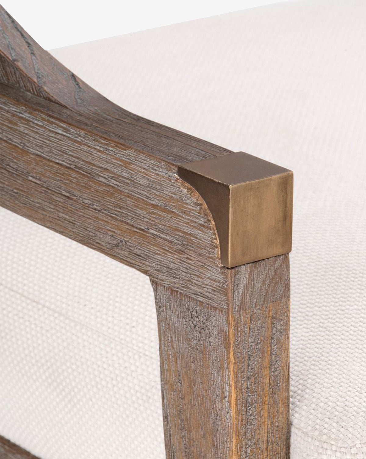 Close-up of the Jensen Dining Chairs solid Cape Lilac Mahogany armrest, featuring a brass corner accent and showcasing its textured wood grain alongside a white upholstered cushion by McGee & Co.