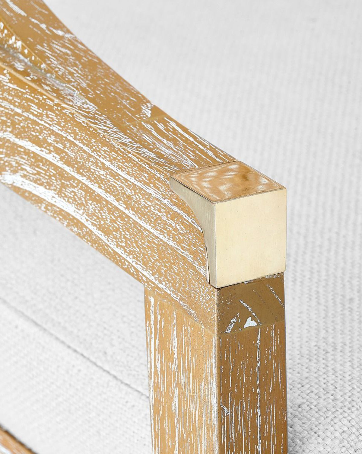 Close-up of the Jensen Dining Chair’s wooden armrest, featuring a distressed light brown finish with white streaks, attached to a textured white upholstered seat and crafted from solid Cape Lilac Mahogany, by McGee & Co.