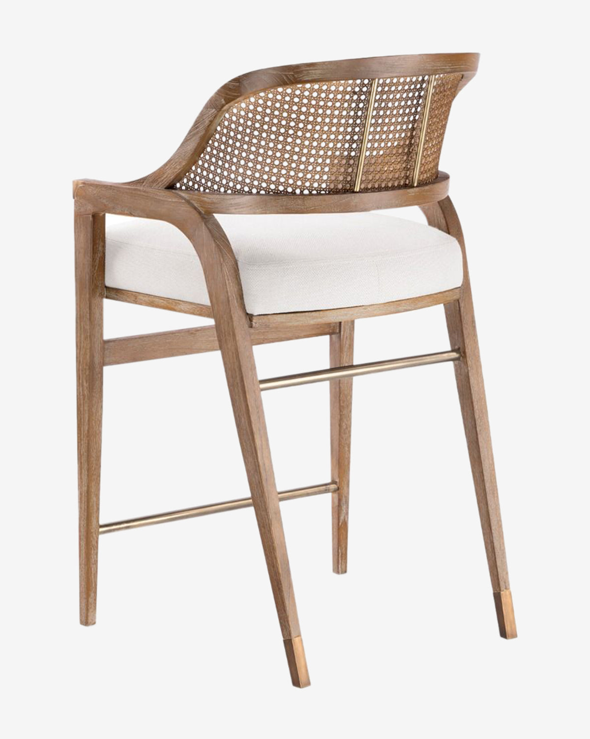 The Jensen Counter Stool has a hand-woven cane back, solid Cape Lilac Mahogany frame, beige cushioned seat, angled legs with a metal footrest and brass-capped feet, all displayed against a white background by McGee & Co.