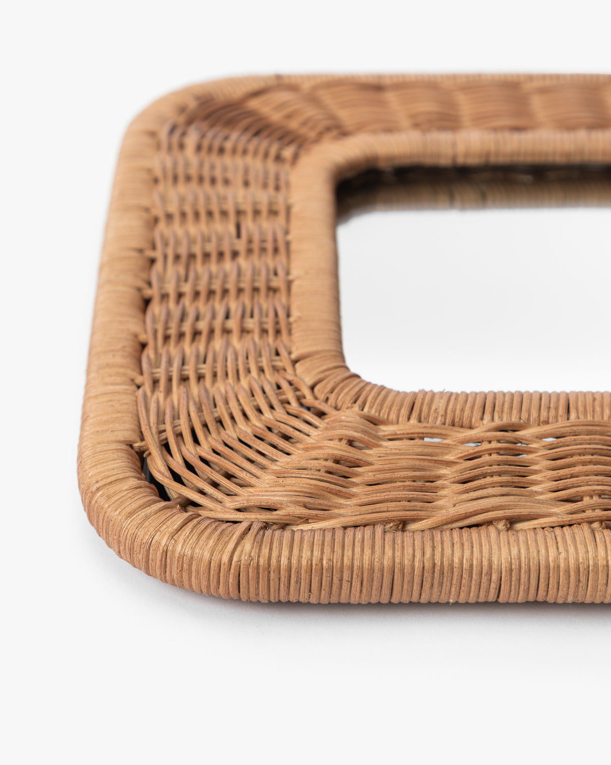 Close-up of a corner of the Jera Shelf Mirrors square, woven rattan frame in natural light brown, highlighting its detailed weaving patterns and texture against a white background by McGee & Co.