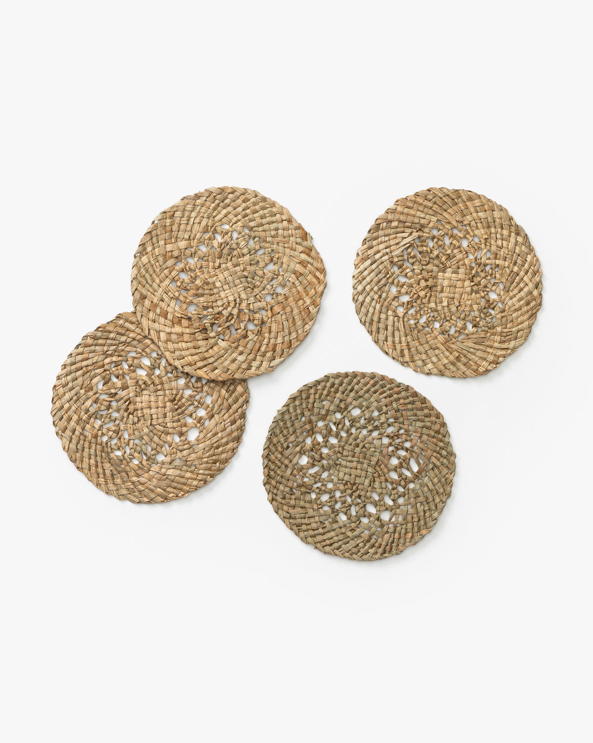 The Joanie Woven Coasters (Set of 4) are round and crafted from mendong grass. Each features unique shades and textures, bringing handmade charm to your table decor. Perfect for adding an organic touch to any setting, by McGee & Co.