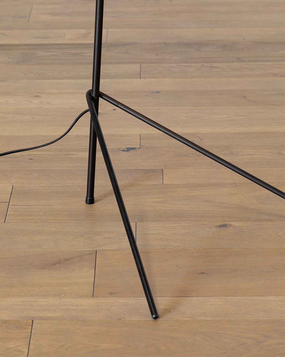 The Johanson Woven Floor Lamp features black metal tripod legs standing on light wood flooring, with a visible black power cord extending from the lamp, by McGee & Co.