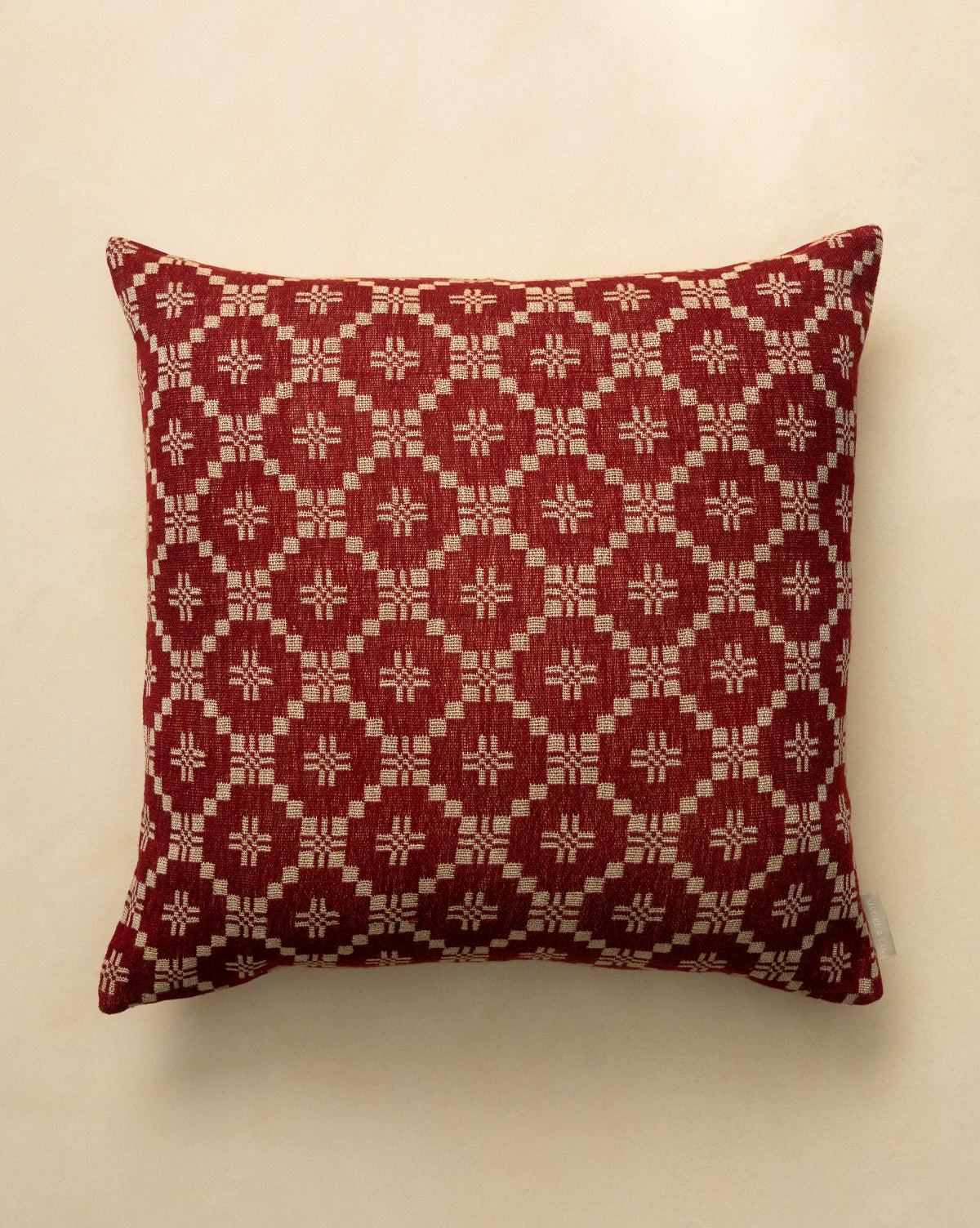 The Jude Pillow Cover is a square, dark red woven cover with a geometric beige diamond and star pattern, shown on a light beige surface, by McGee & Co.