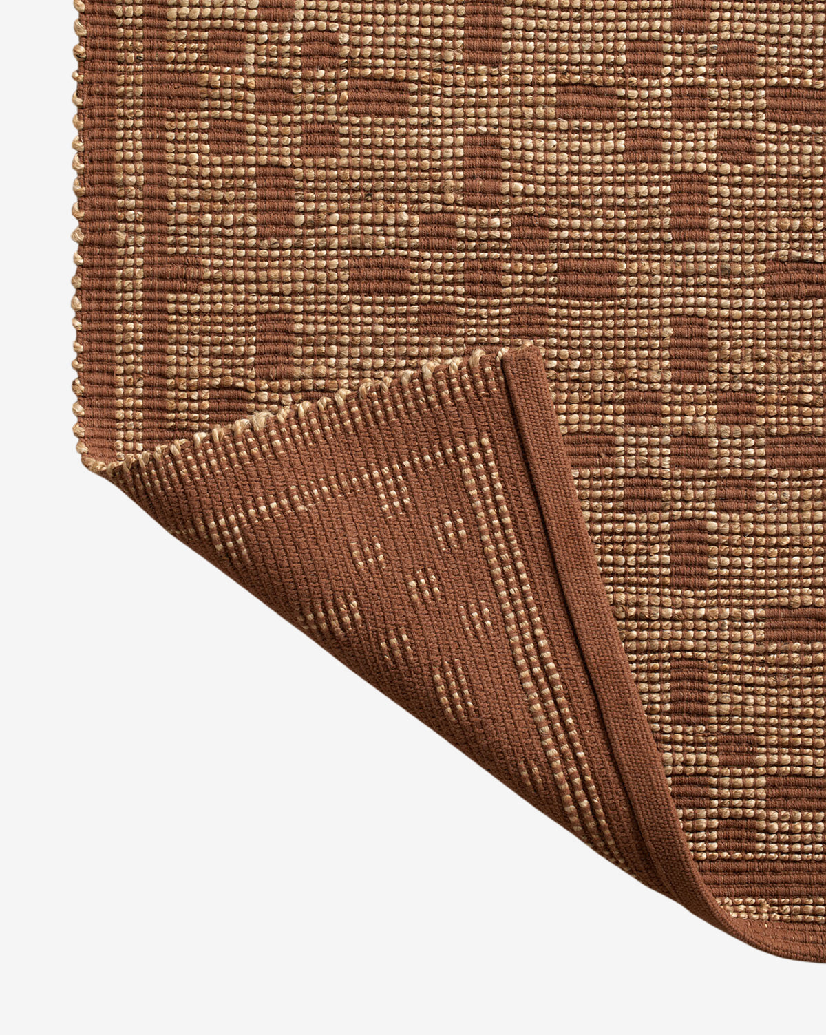 A close-up of the Judy Spice Jute Rug Collection No. 7 showcases its handwoven geometric square pattern, with one corner folded to display the underside and neatly finished edge, by McGee & Co.