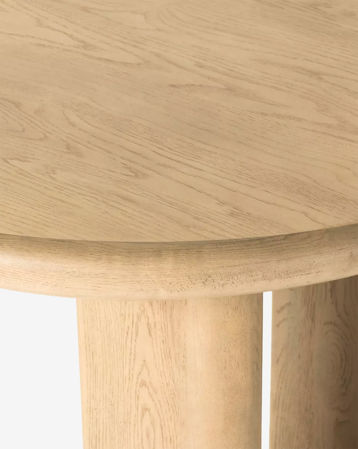 Close-up of the Juliana Extension Dining Table, featuring a round solid oak top with light wood grain and two thick, cylindrical legs beneath its modern edge design, by McGee & Co.