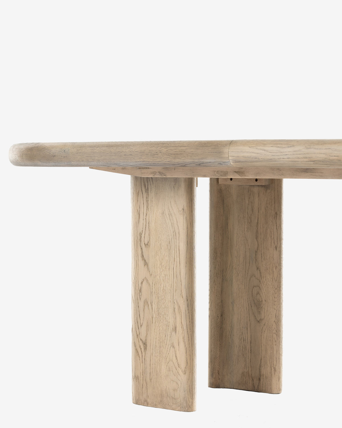 A close-up side view of the Juliana Extension Dining Table, featuring a thick, rounded solid oak top and two wide rectangular legs, highlighting its light natural wood grain and modern design against a plain white background, by McGee & Co.