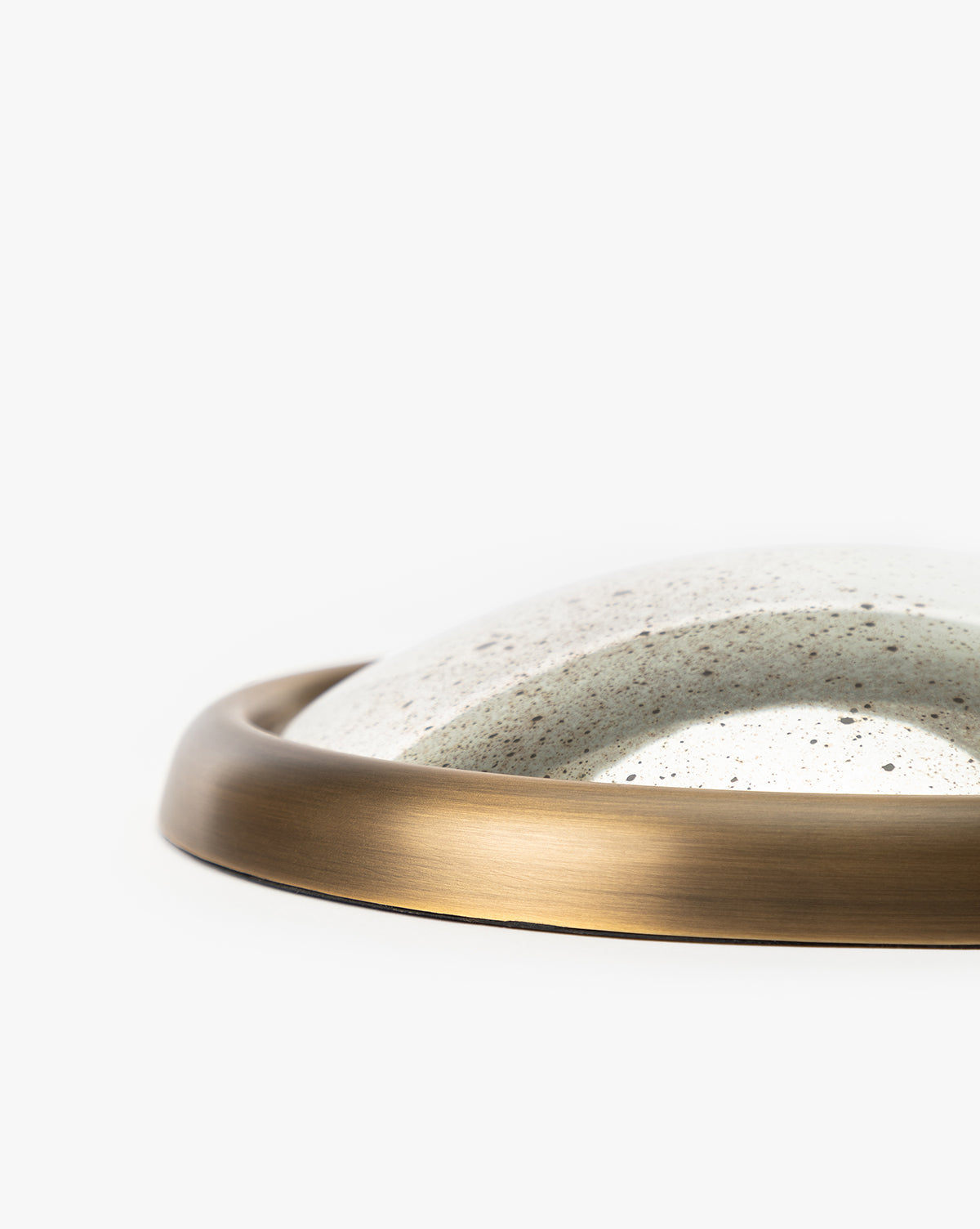 A close-up of the Juliette Convex Antiqued Mirror features its round, speckled white ceramic center, surrounded by a smooth vintage brass frame, all set against a plain white background, by McGee & Co.